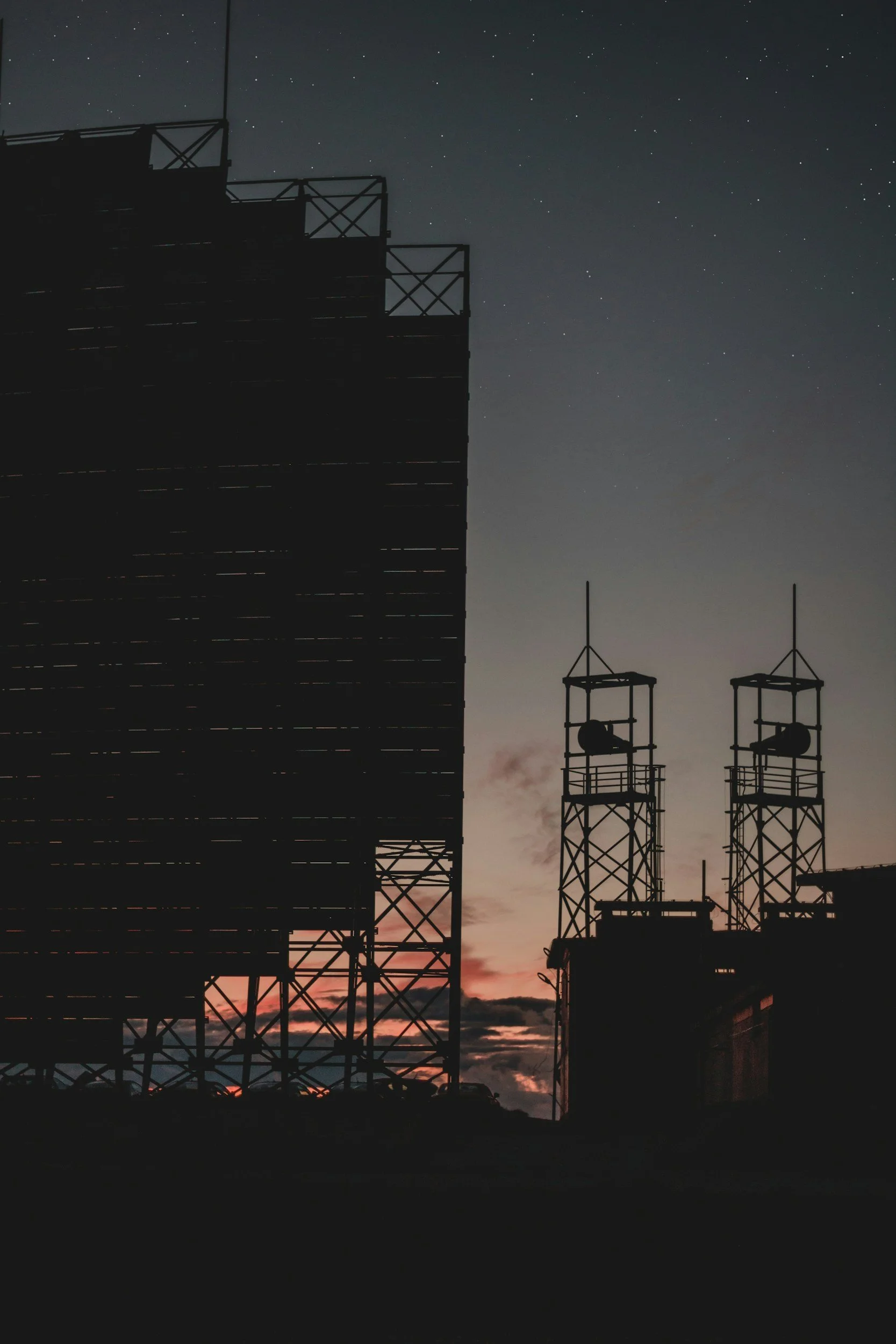 Silhouette of a large building and communication towers against a twilight sky with stars, with a faint pink and orange sunset on the horizon.