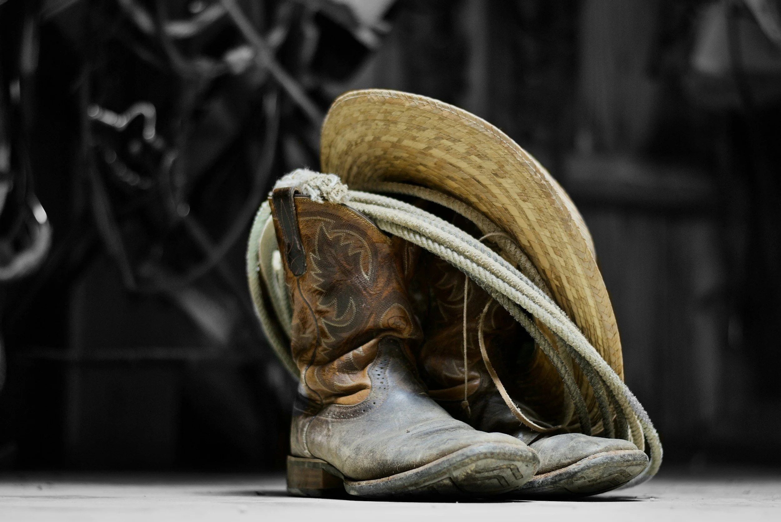 A pair of cowboy boots, with a straw cowboy hat resting on top, sitting on a wooden surface.