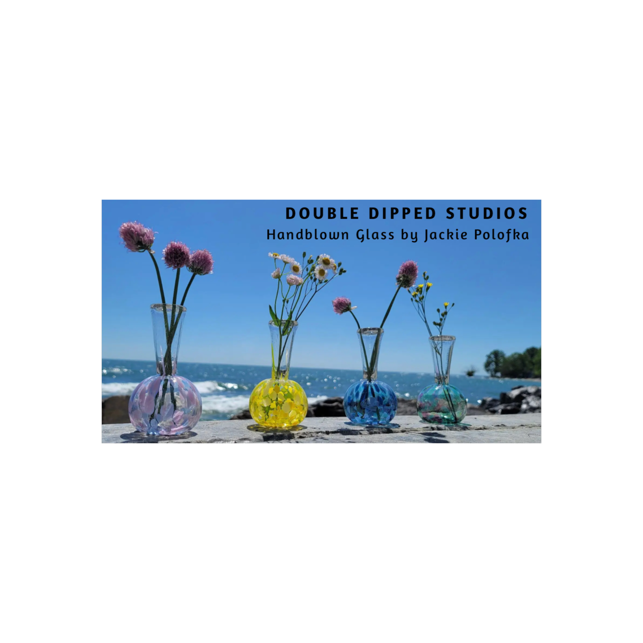Colorful handblown glass vases with flowers on a beach, ocean and blue sky background.