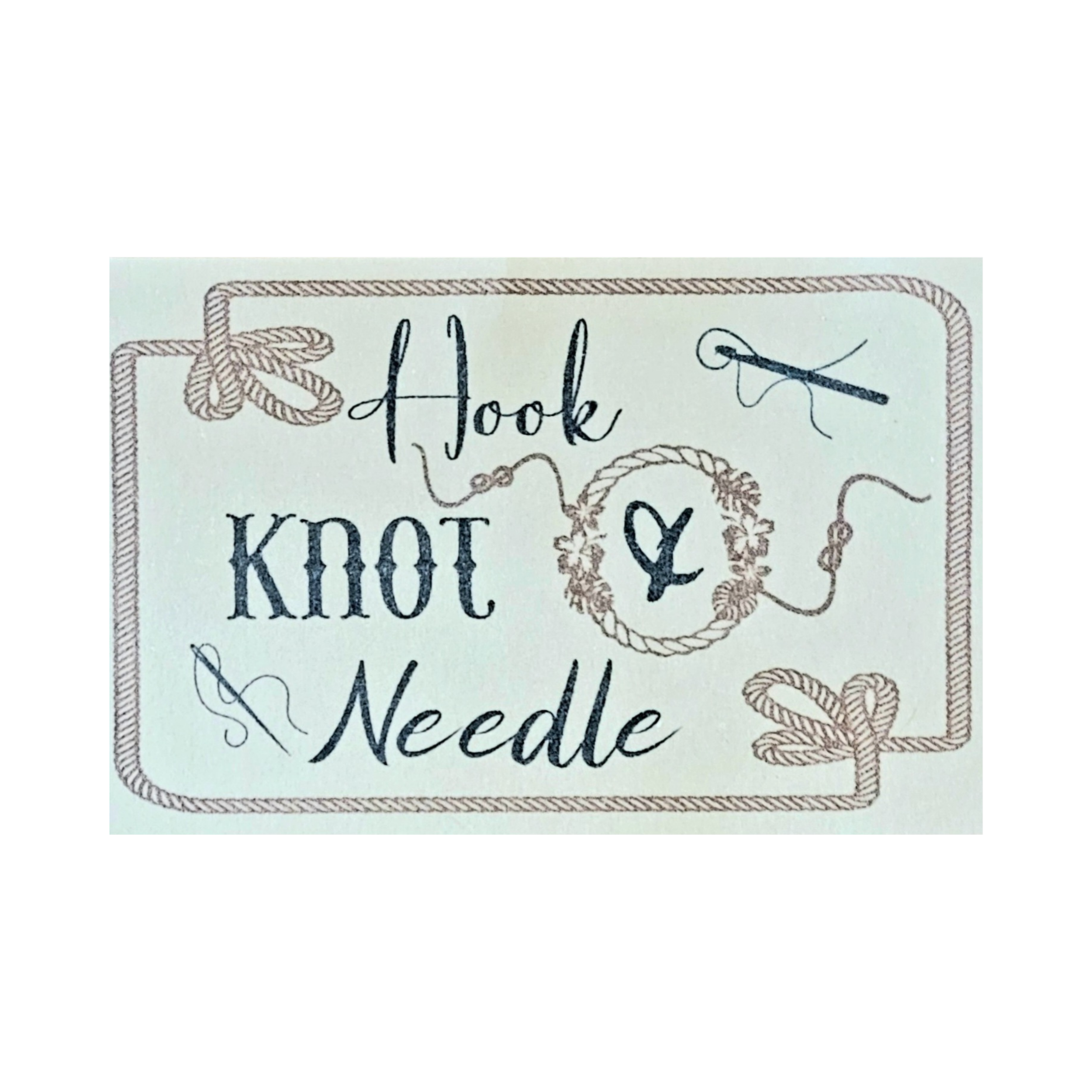 Decorative sign with the words "Hoot, Knook, &" in black cursive lettering, surrounded by a rope border and images of knitting needles, yarn, and floral elements.