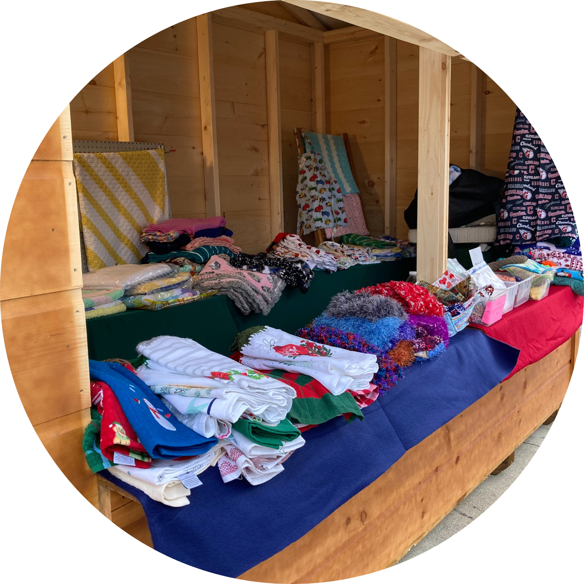 A wooden display shelf filled with folded clothes and fabric items, some with Christmas or holiday themes, in a store or market setting.