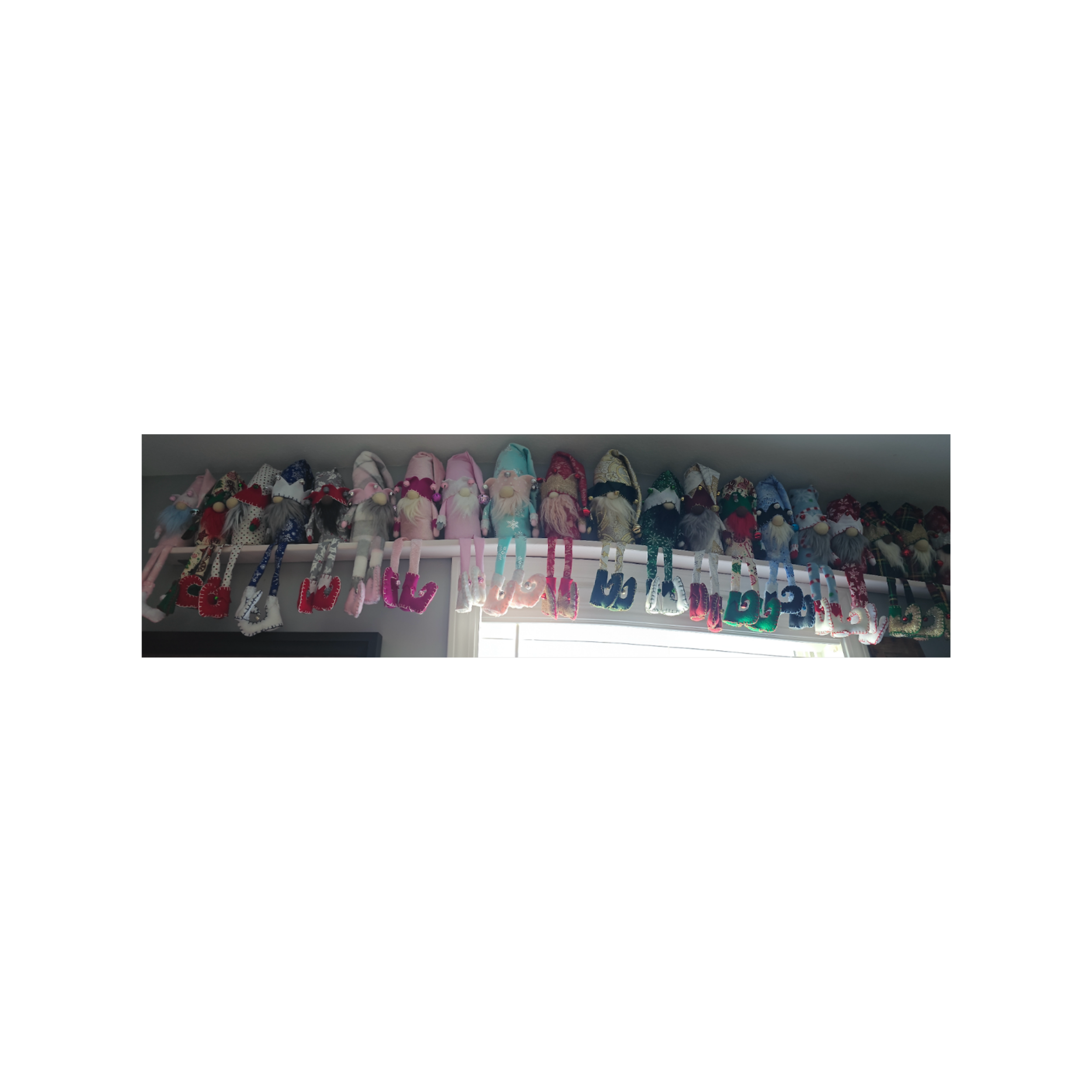 Colorful fabric Christmas gnome figures hanging on a string above a window with blinds, with the text 'Have a Holly Jolly Christmas' in pink and multicolored letters.