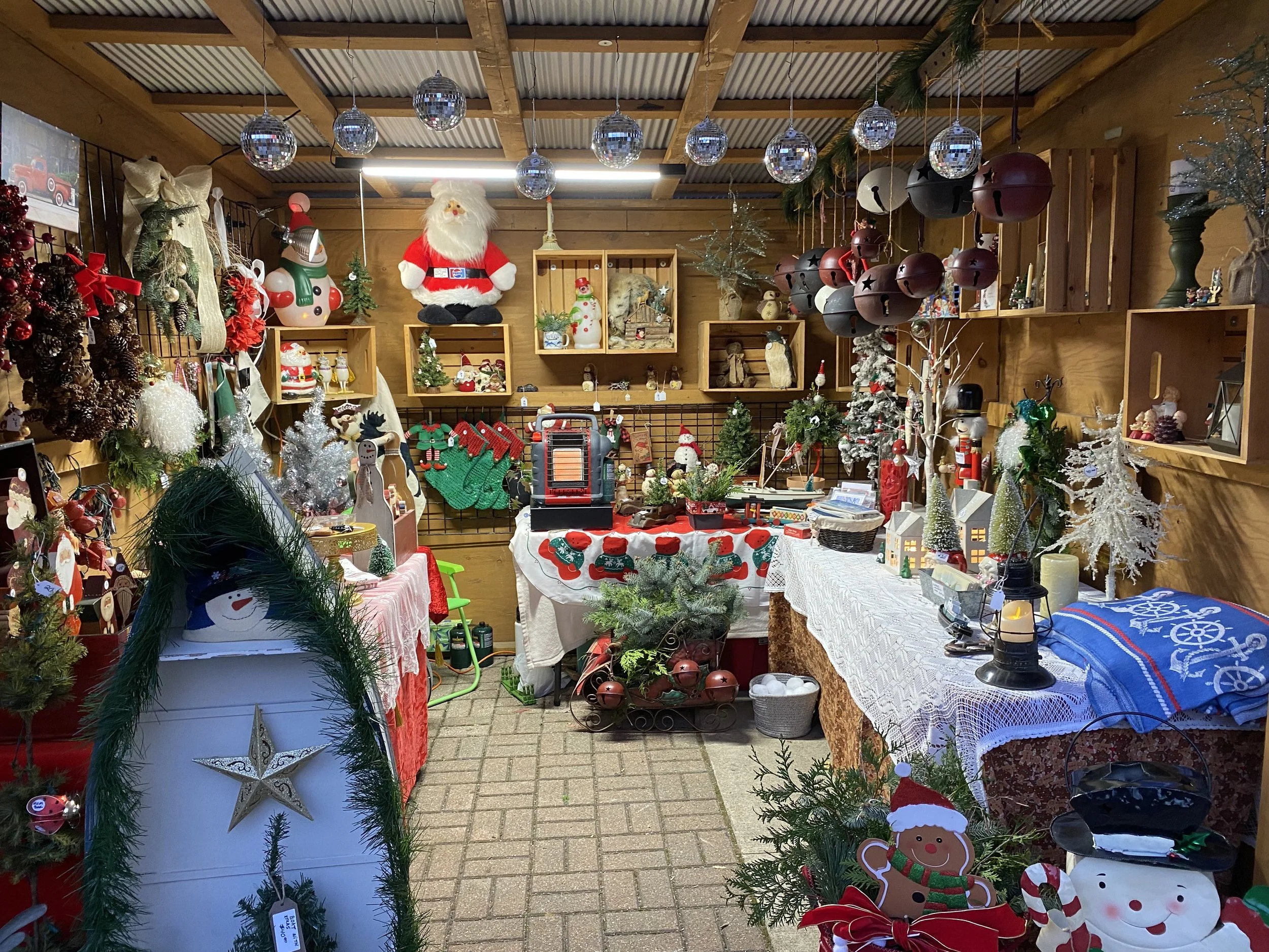 A Christmas-themed market stall decorated with various holiday decorations, figurines, and ornaments, including Santa Claus, reindeer, and snowmen, with disco balls hanging from the ceiling.