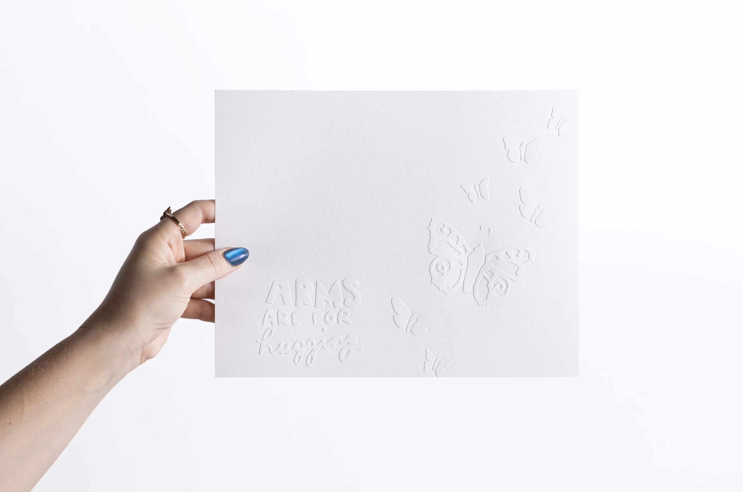 White embossed watercolor paper artwork featuring butterfly flutter and phrase that says Arms are for Hugging.