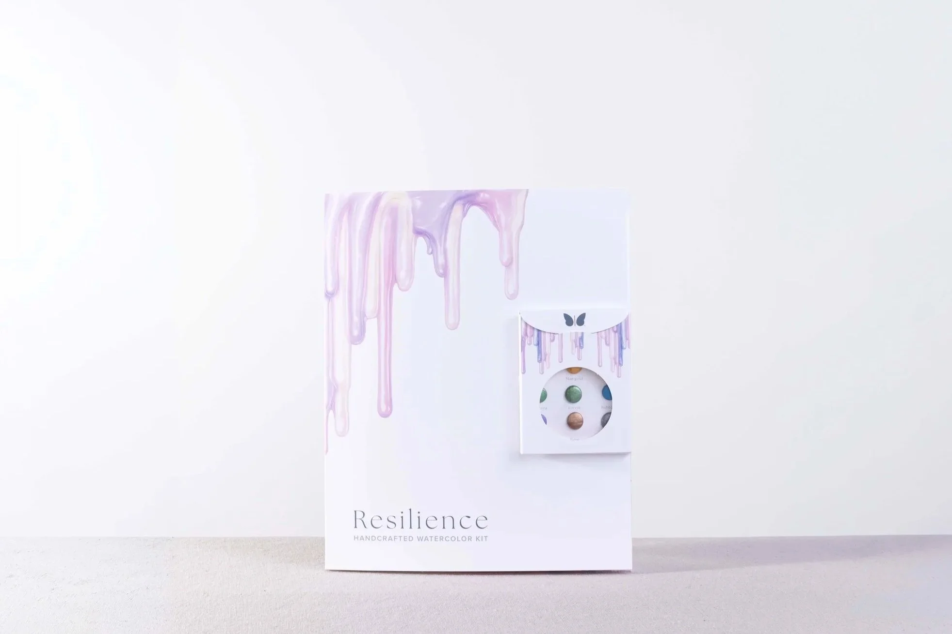 Front-facing view of the completed Resilience watercolor kit packaging featuring lavender paint drips and a mounted watercolor palette.