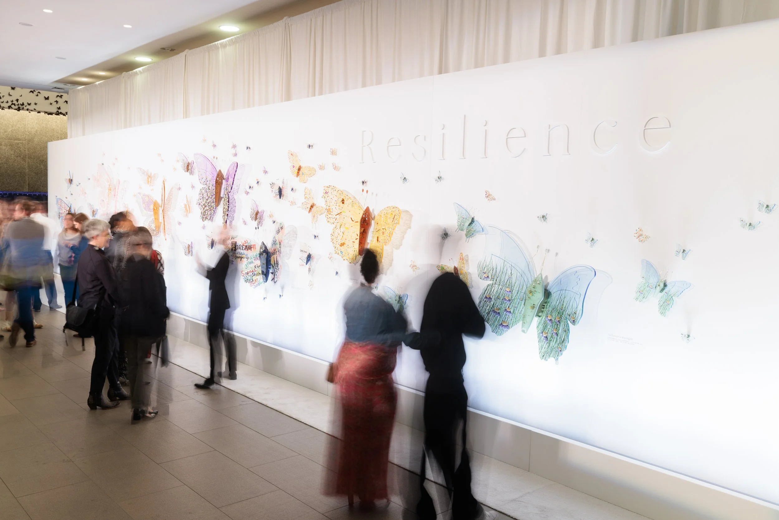 People standing in front of a large wall display with butterflies and the word 'Resilience' in the background.