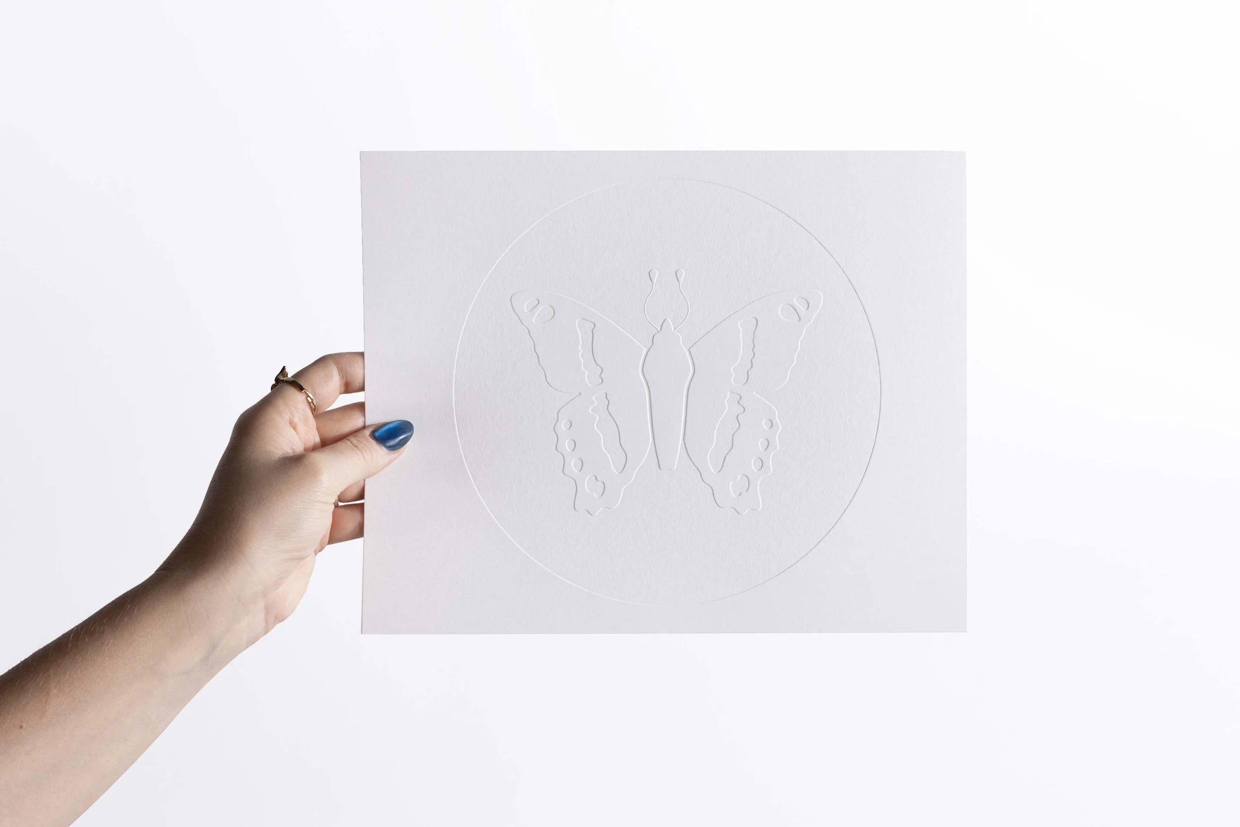 Close-up of an embossed circular butterfly design on white paper.