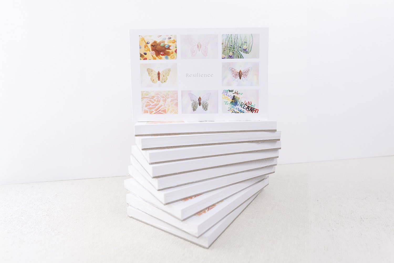 Stack of Resilience Postcard Books featuring a colorful grid of butterfly artwork on the cover, created by Butterfly Art Collective.