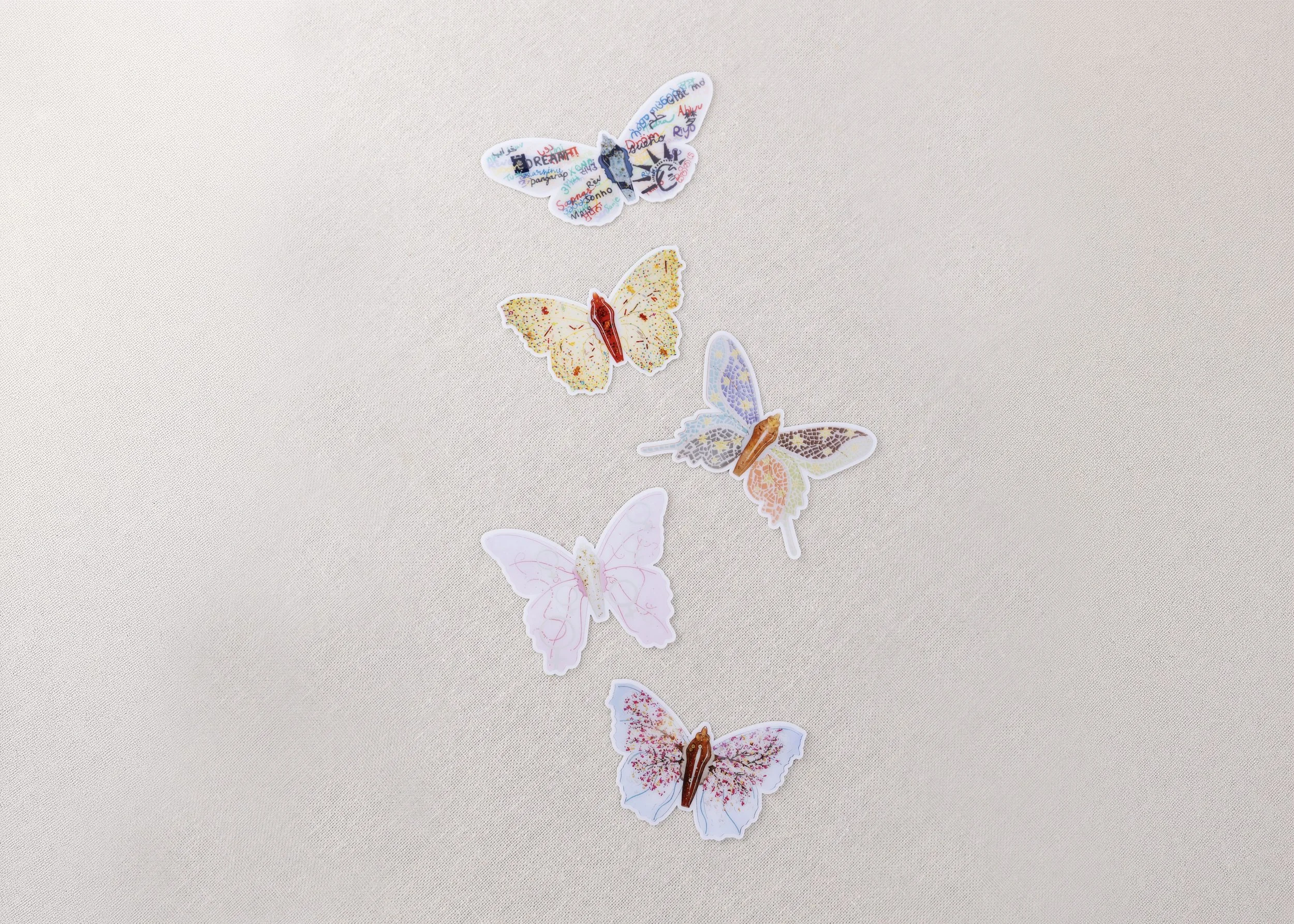 Five colorful butterfly-shaped vinyl stickers from the Resilience collection arranged on a canvas background, each featuring a unique artistic design.