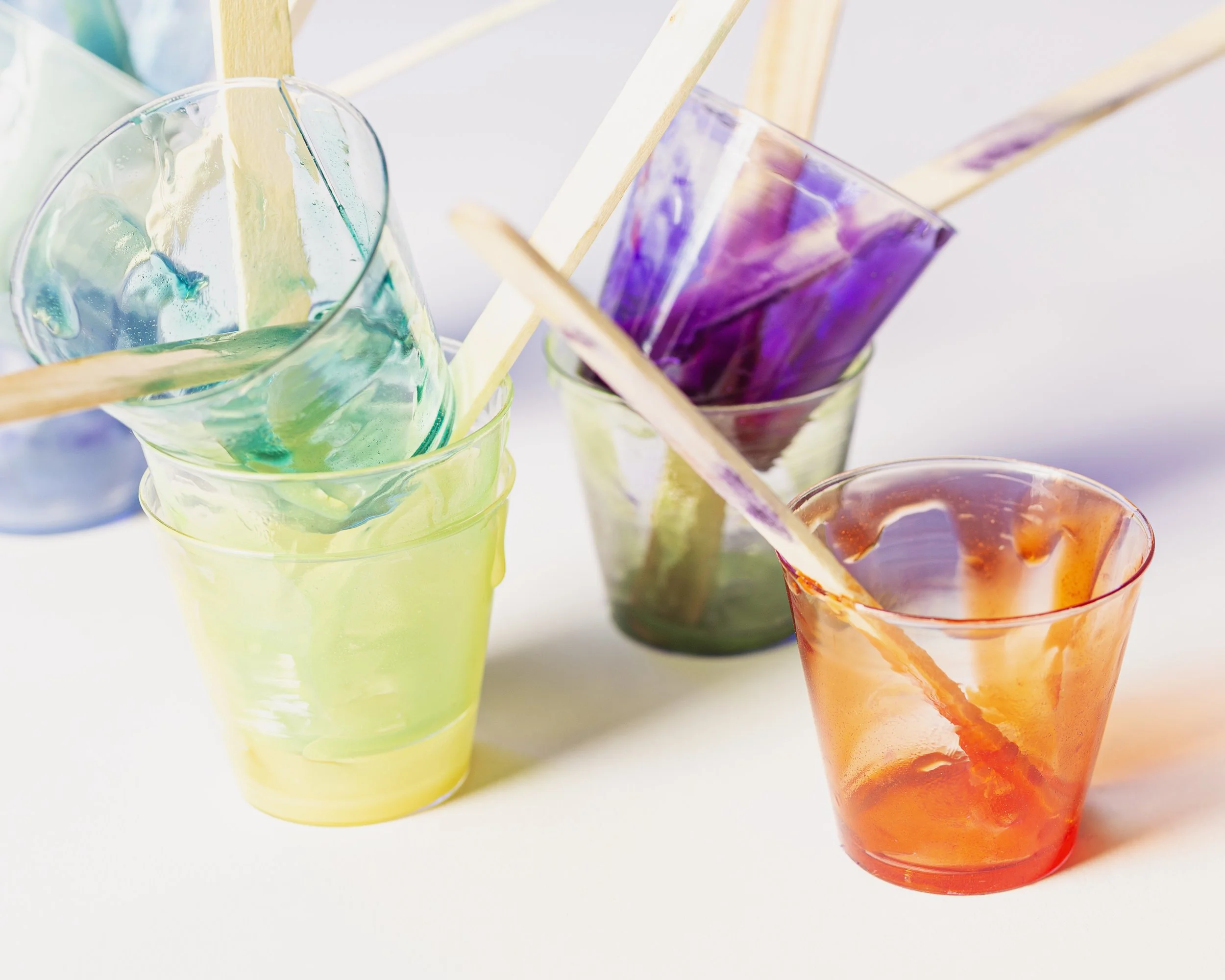 Colorful glasses of resin with popsicle sticks resting on top.