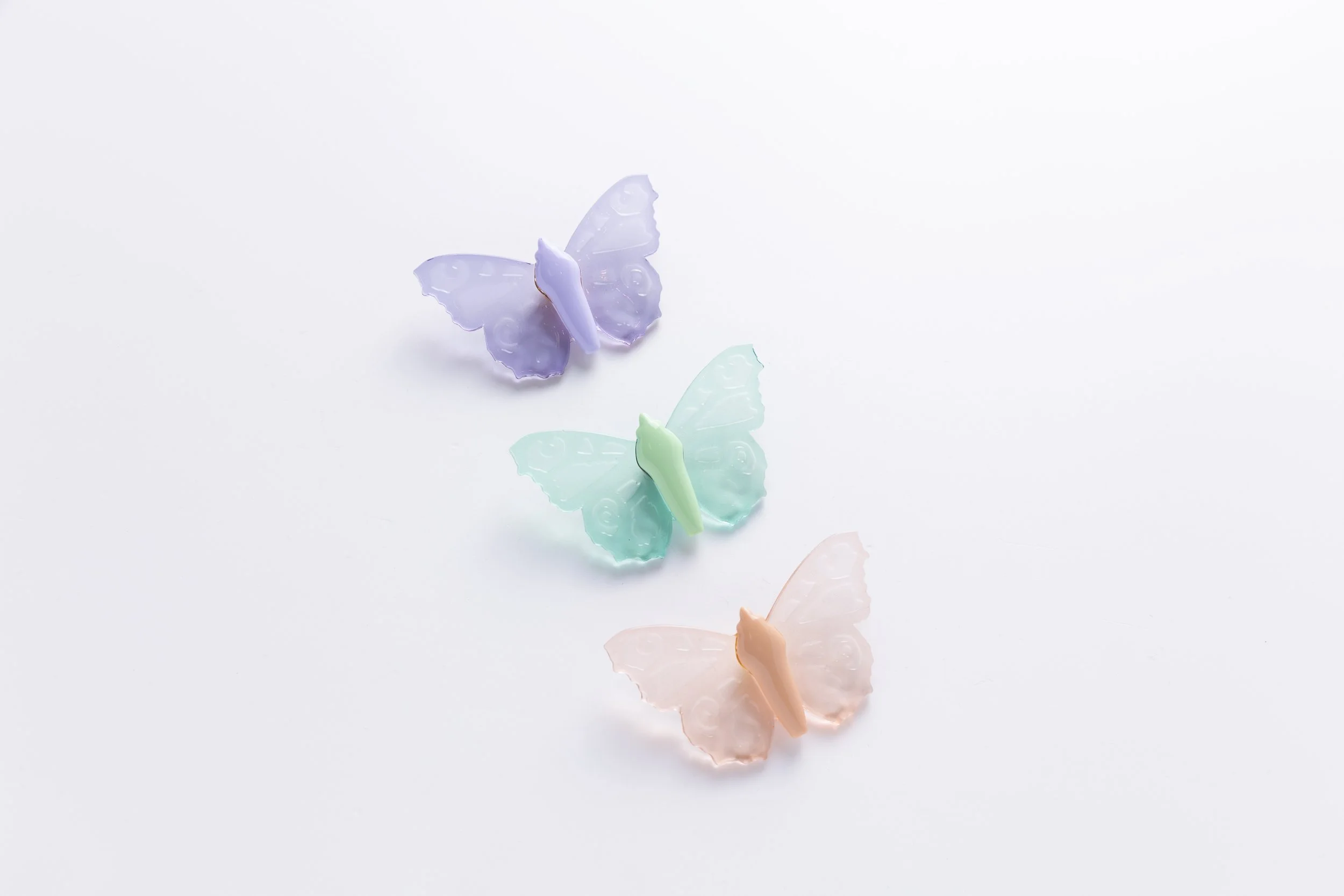 Three handcrafted glass-like soft resin butterfly pins by Butterfly Art Collective in Twilight Glass lavender, Sea Glass aqua, and Desert Glass peach.