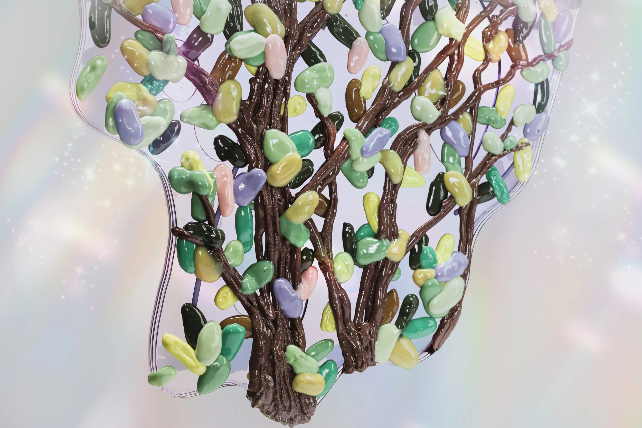Close-up of a resin butterfly sculpture with a tree with a brown trunk and multicolored leaves resembling candies, on a white surface.
