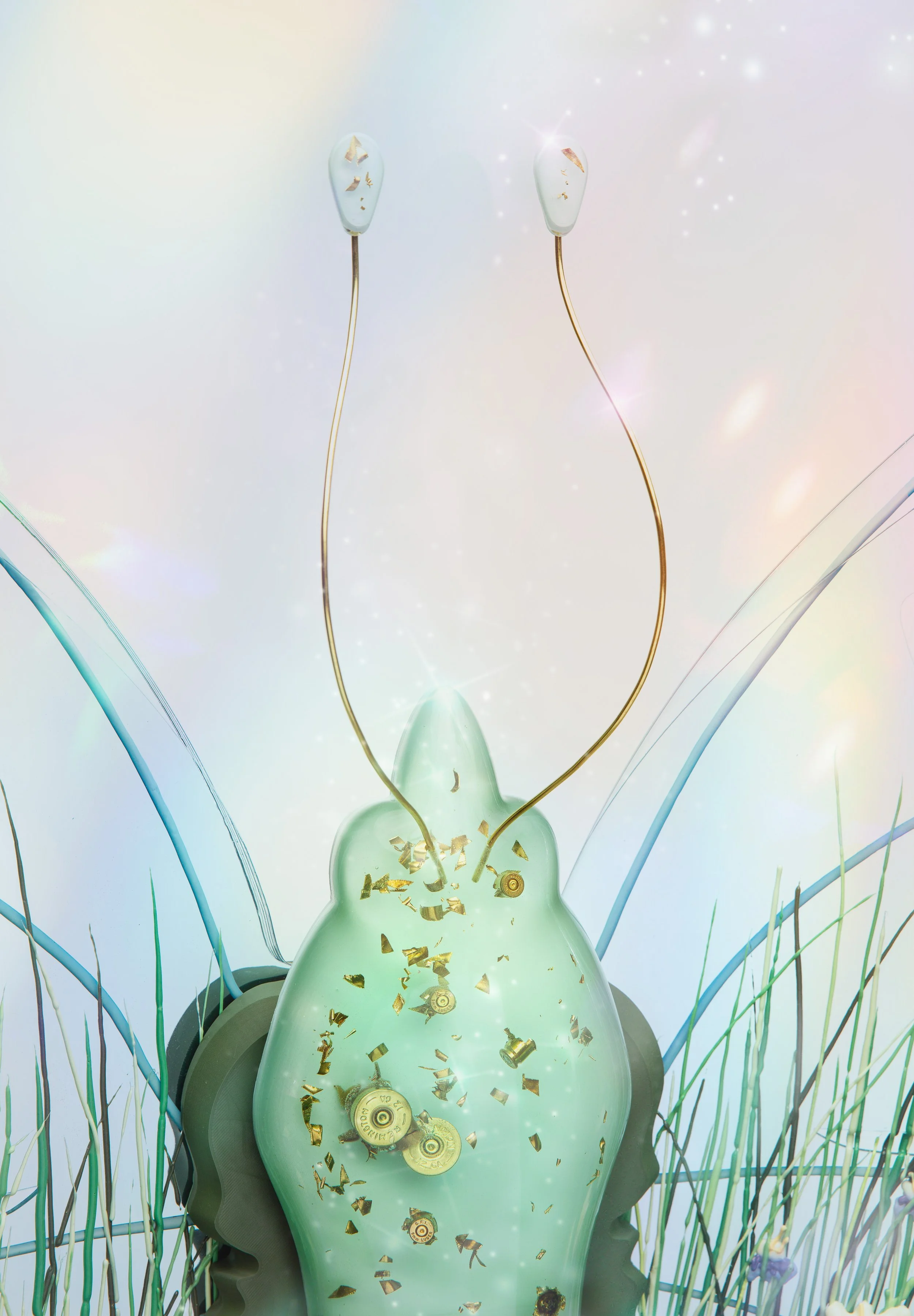 Decorative resin butterfly thorax with embedded shredded bullet shell casings, surrounded by tall blue and green grasses, abstract light background.