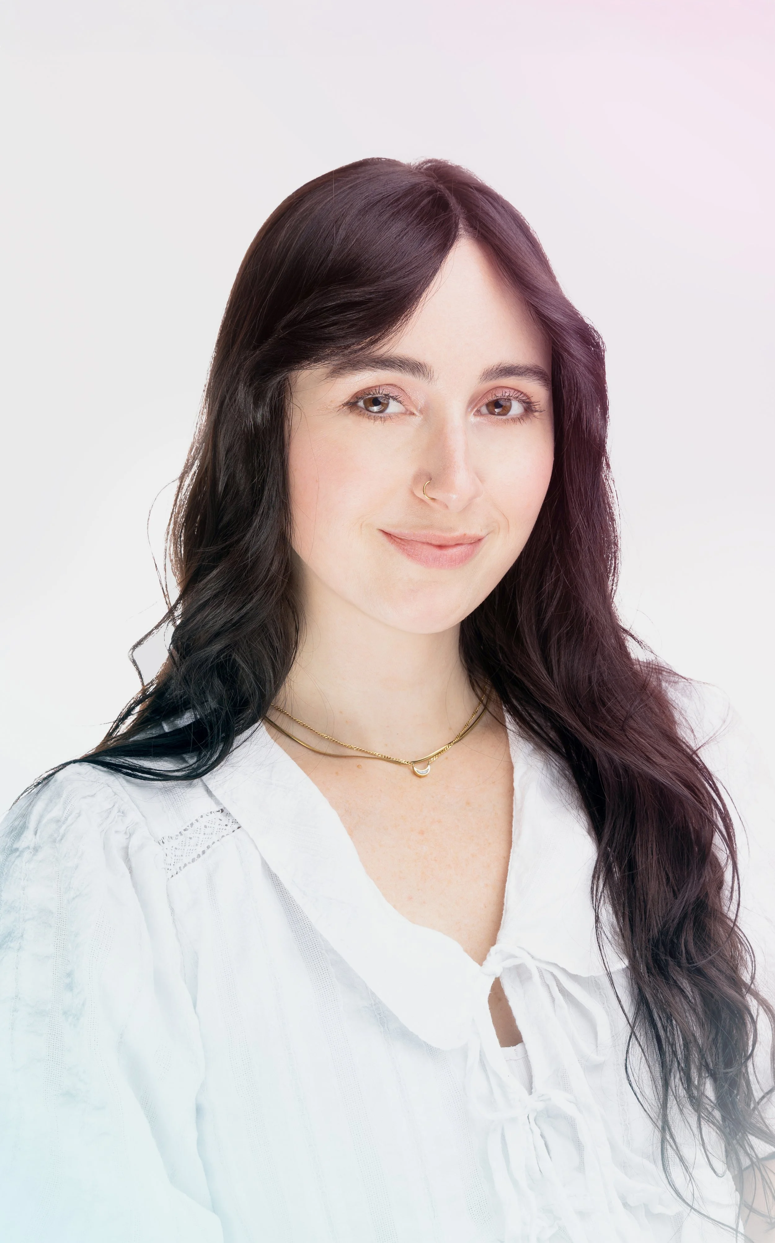 Portrait of Audrey Wilbourn, with long dark wavy hair and light skin, smiling gently, wearing a white blouse and a gold necklace, against a plain light background.