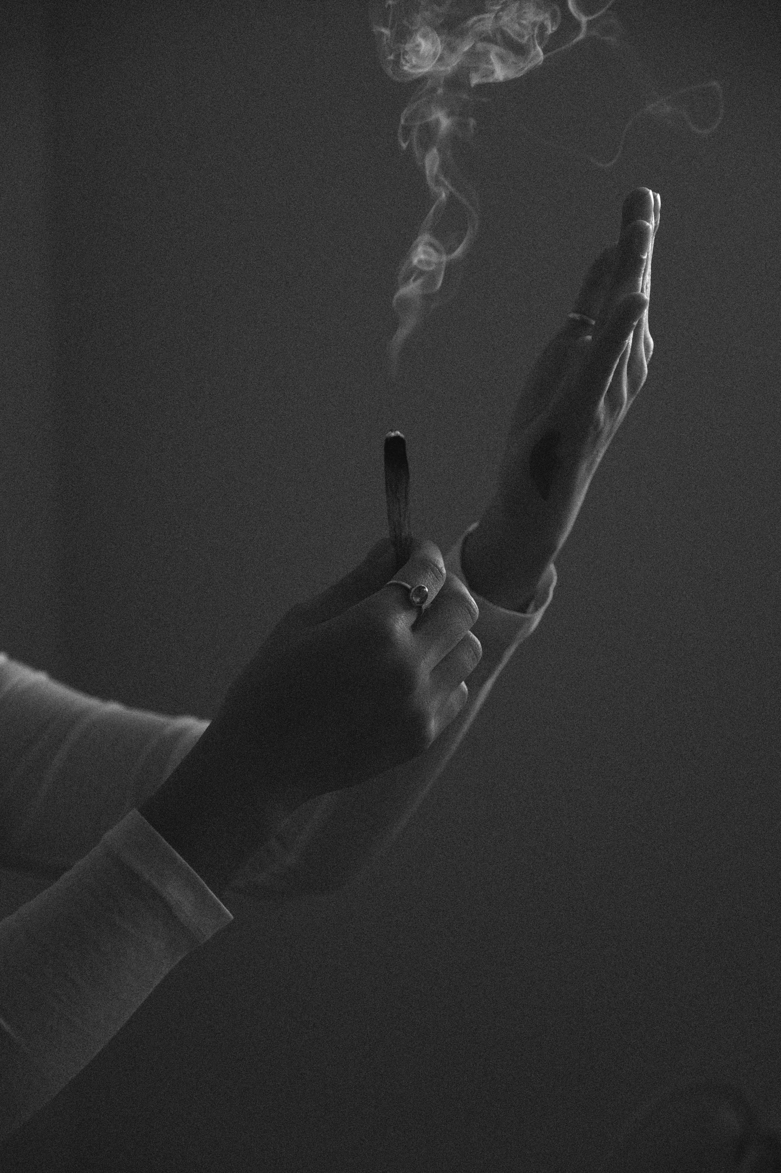 Black and white photo of a person holding a cigarette with smoke rising, shielding their face with the other hand.