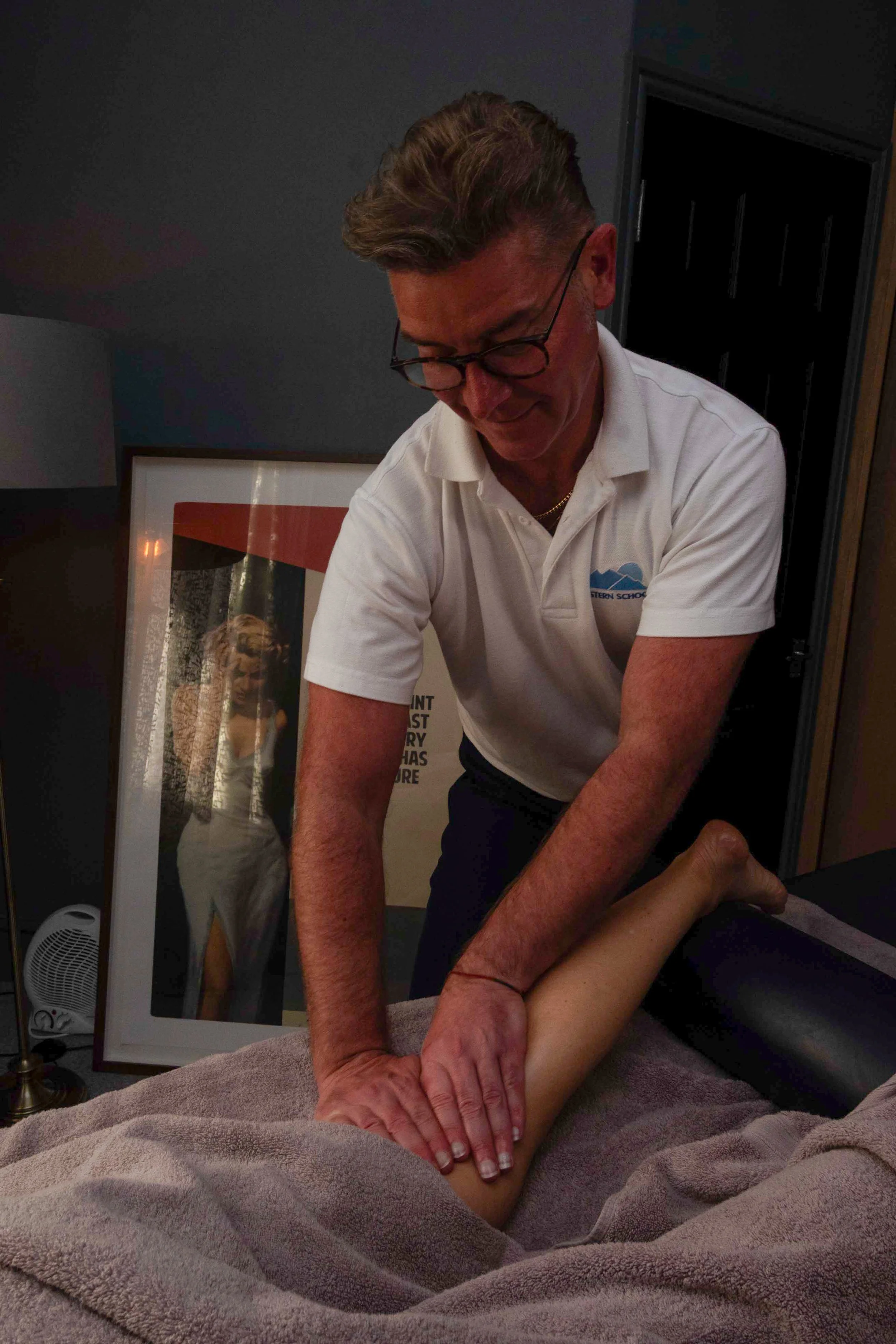 A man giving a massage to a person's leg on a massage table in a dimly lit room.