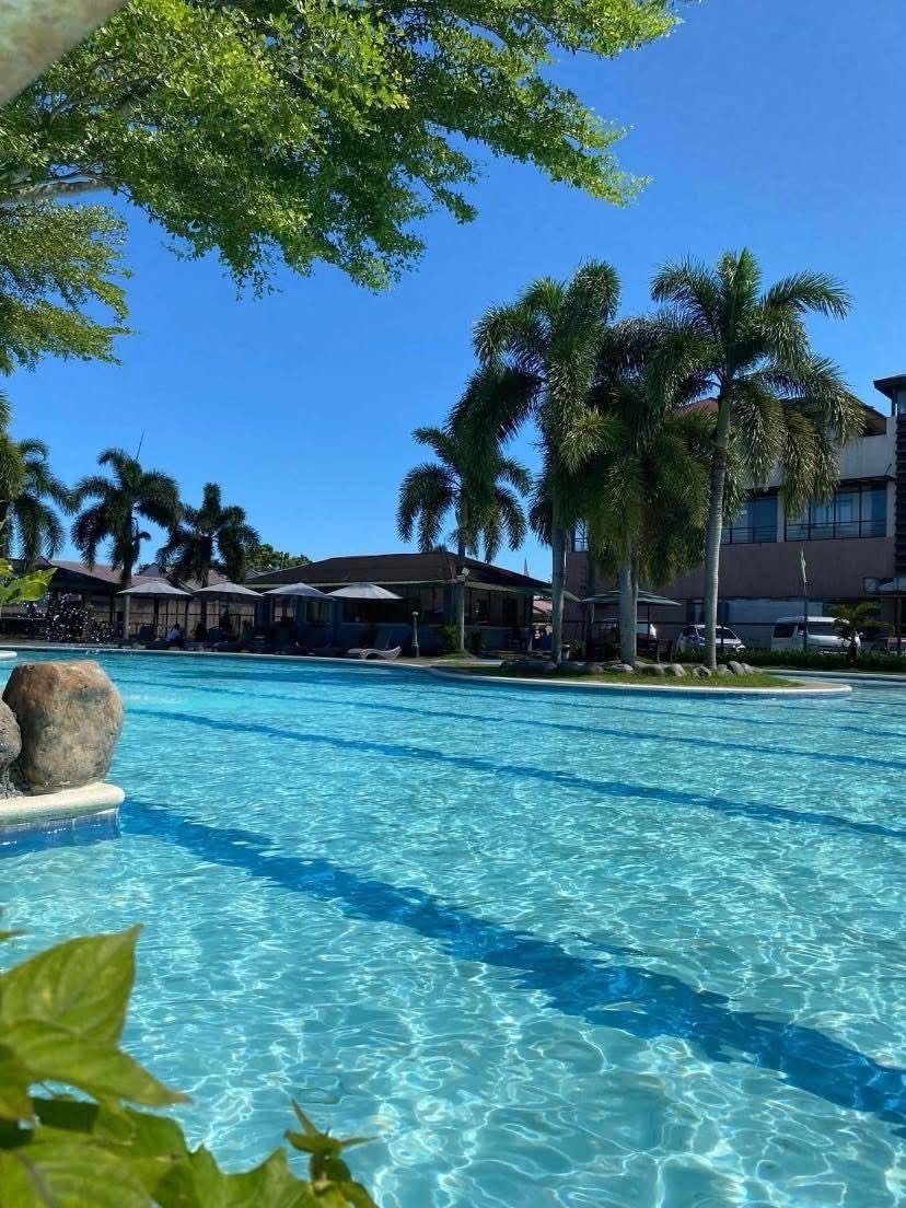 A clear blue swimming pool with palm trees and a building in the background on a sunny day.