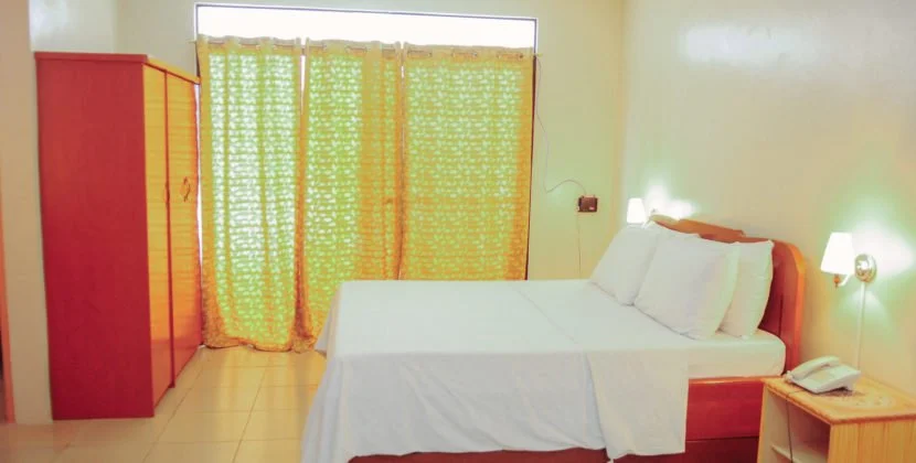 Modern living and dining area with brown furniture, glass coffee table, kitchen in the background, and a chandelier.