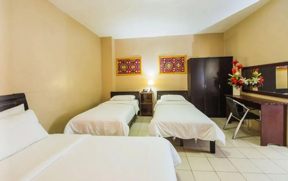 Hotel room with three beds, a wardrobe, a desk with a chair, wall art, and a bedside lamp.