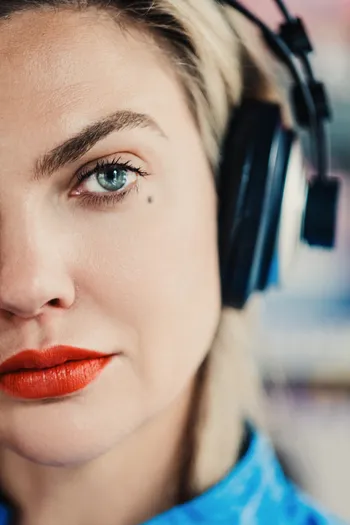 Close-up of a woman wearing headphones with a neutral expression, showing her eye, eyebrow, and red lipstick.