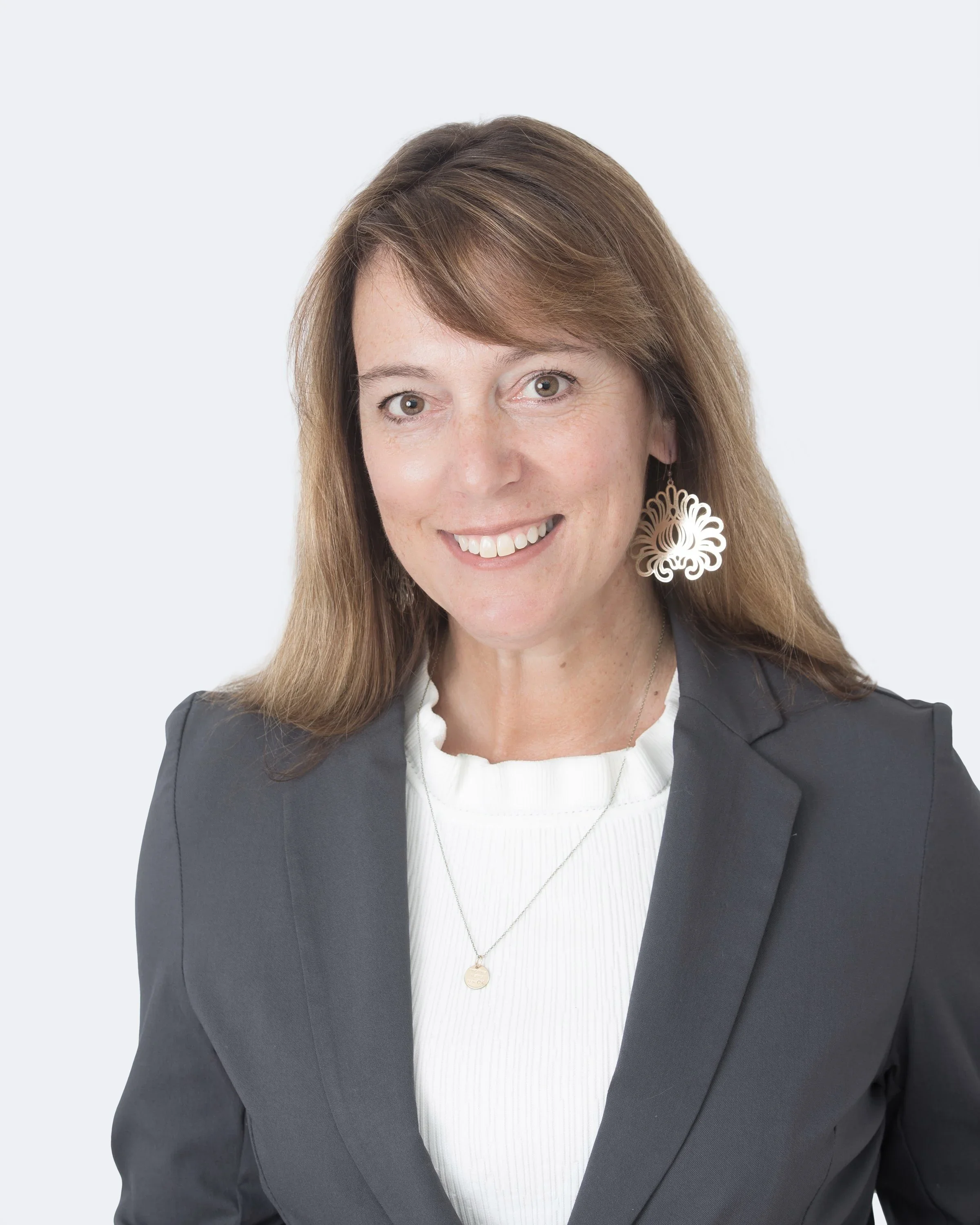A woman with shoulder-length brown hair wearing a black blazer, white top, and large decorative earrings, smiling at the camera.