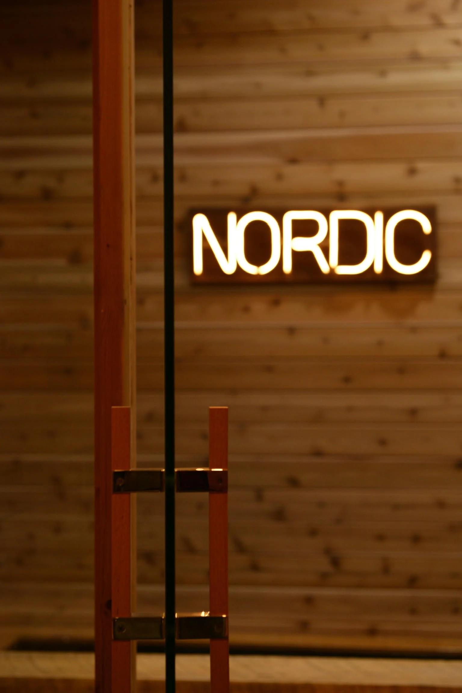 Glowing Nordic neon sign viewed through cedar sauna glass door at Nordic on Nine in New Windsor NY