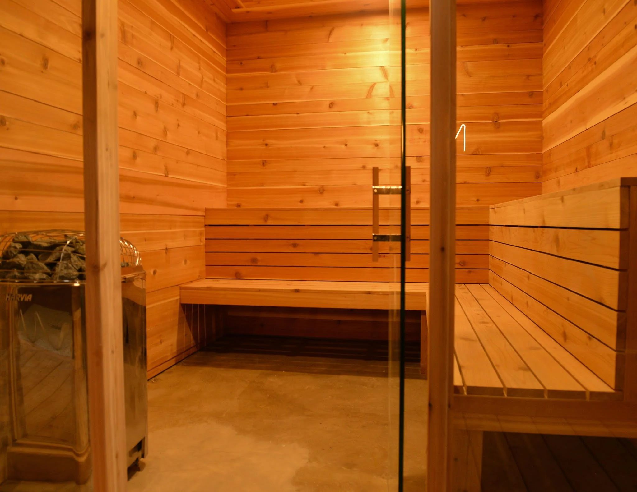 Cedar-lined Finnish sauna interior with Harvia stone heater and glass door at Nordic on Nine in New Windsor NY