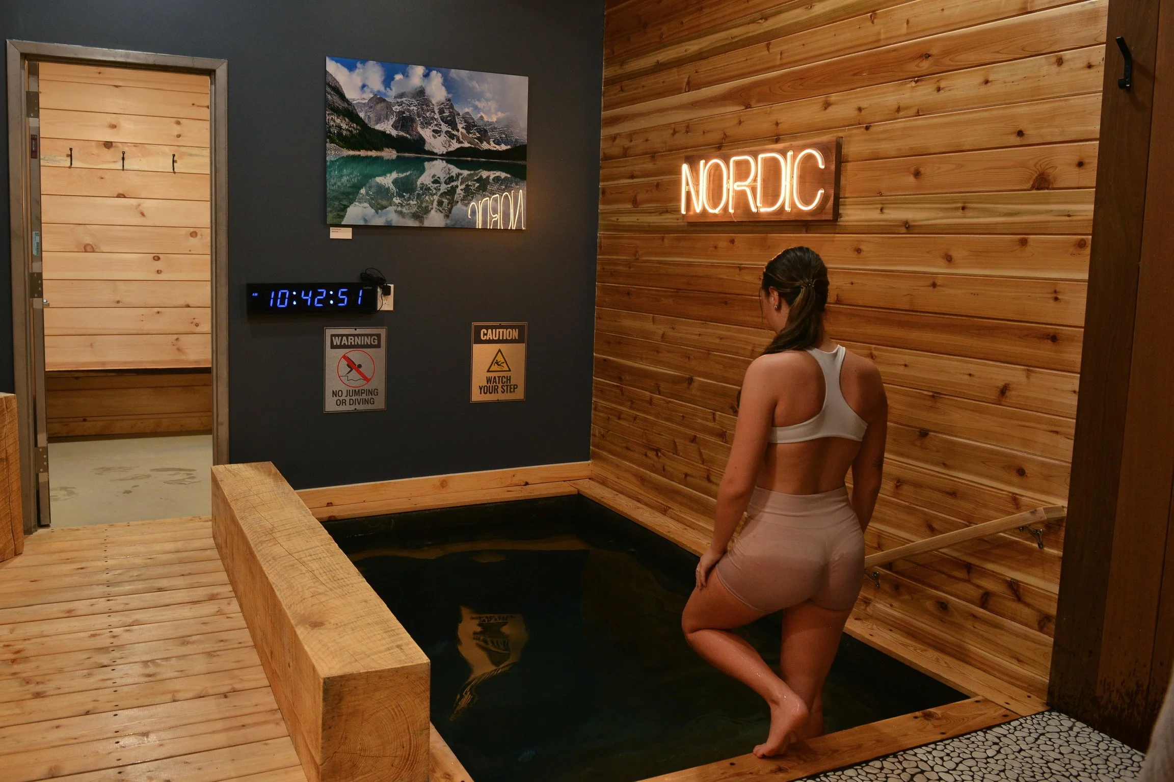 Woman stepping into the cold plunge pool in the fire room area at Nordic on Nine sauna spa in New Windsor NY