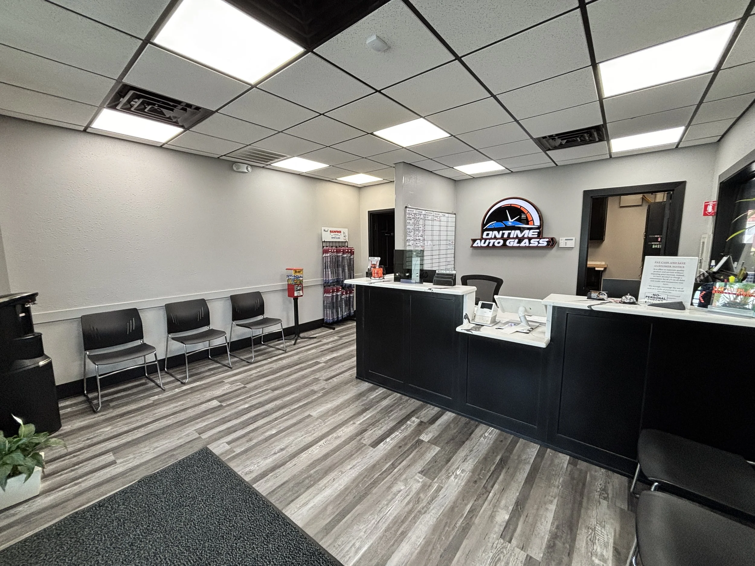 Reception area of Ontime Auto Glass with a black counter, chairs on the left, and a sign on the wall displaying the company logo.