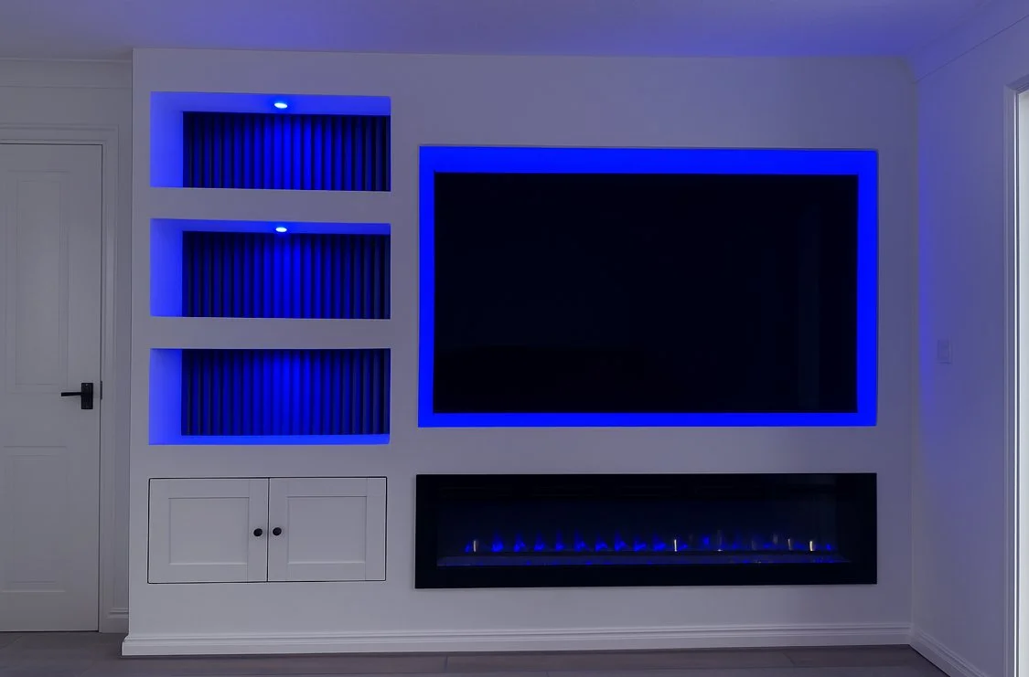 Modern living room wall with a large flat-screen TV surrounded by blue LED backlighting, a built-in electric fireplace, and storage cabinets.