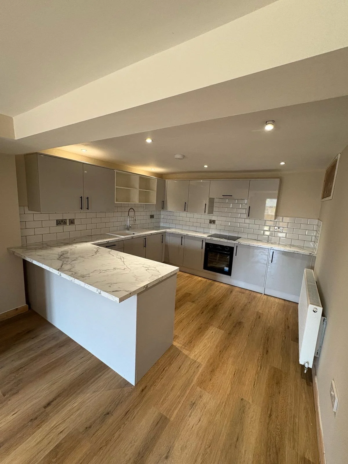 Modern kitchen with gray cabinets, white subway tile backsplash, marble countertop on island, wooden flooring, and ceiling recessed lighting.