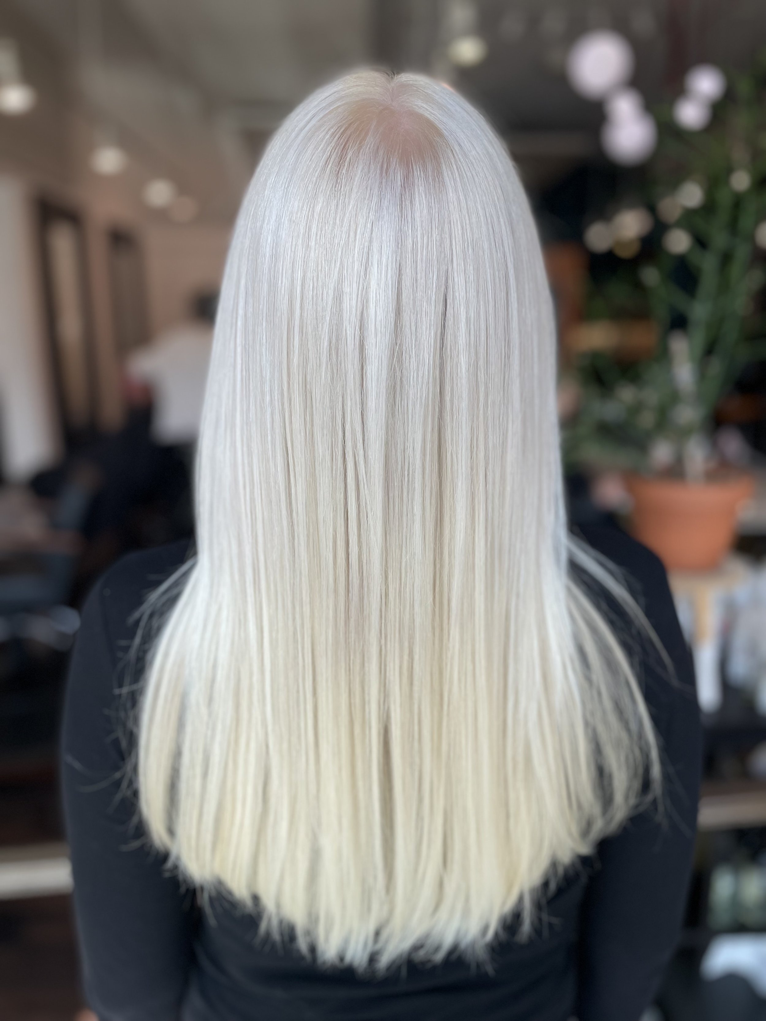Long, straight platinum blonde hair viewed from the back inside a salon setting.