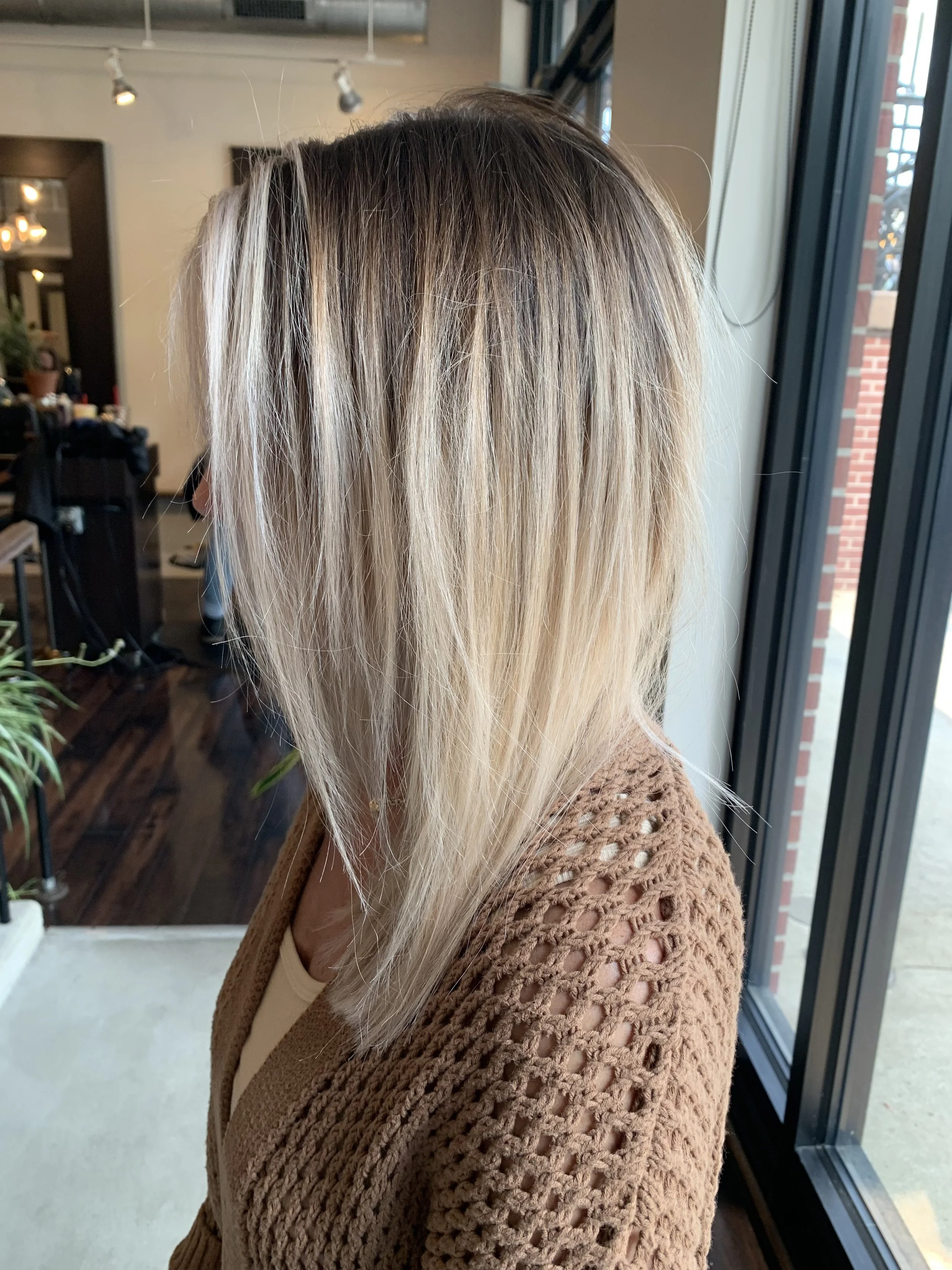 Woman with shoulder-length blonde hair in a salon, wearing a brown crocheted sweater.