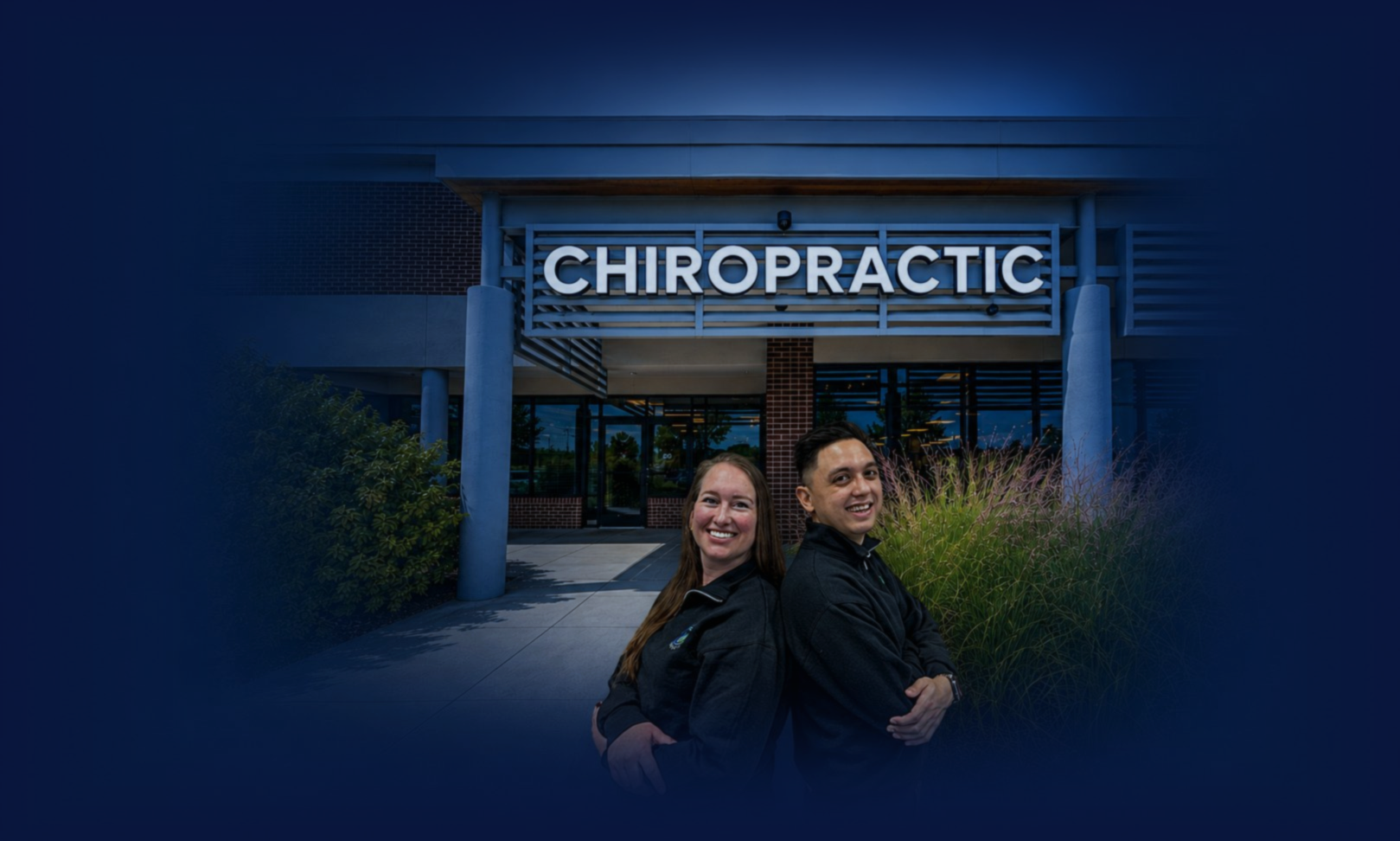 Two smiling individuals standing back-to-back outside a building with a sign that reads 'Chiropractic'.