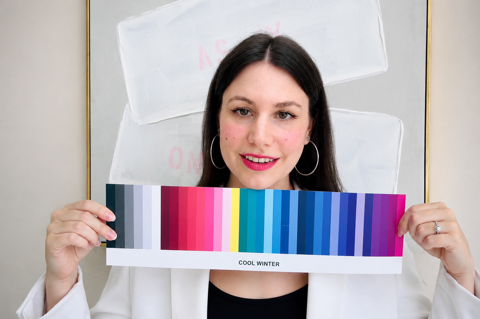 A woman with dark hair, wearing hoop earrings and a white blazer, holds a color swatch labeled "Cool Winter" in a luxurious living room.