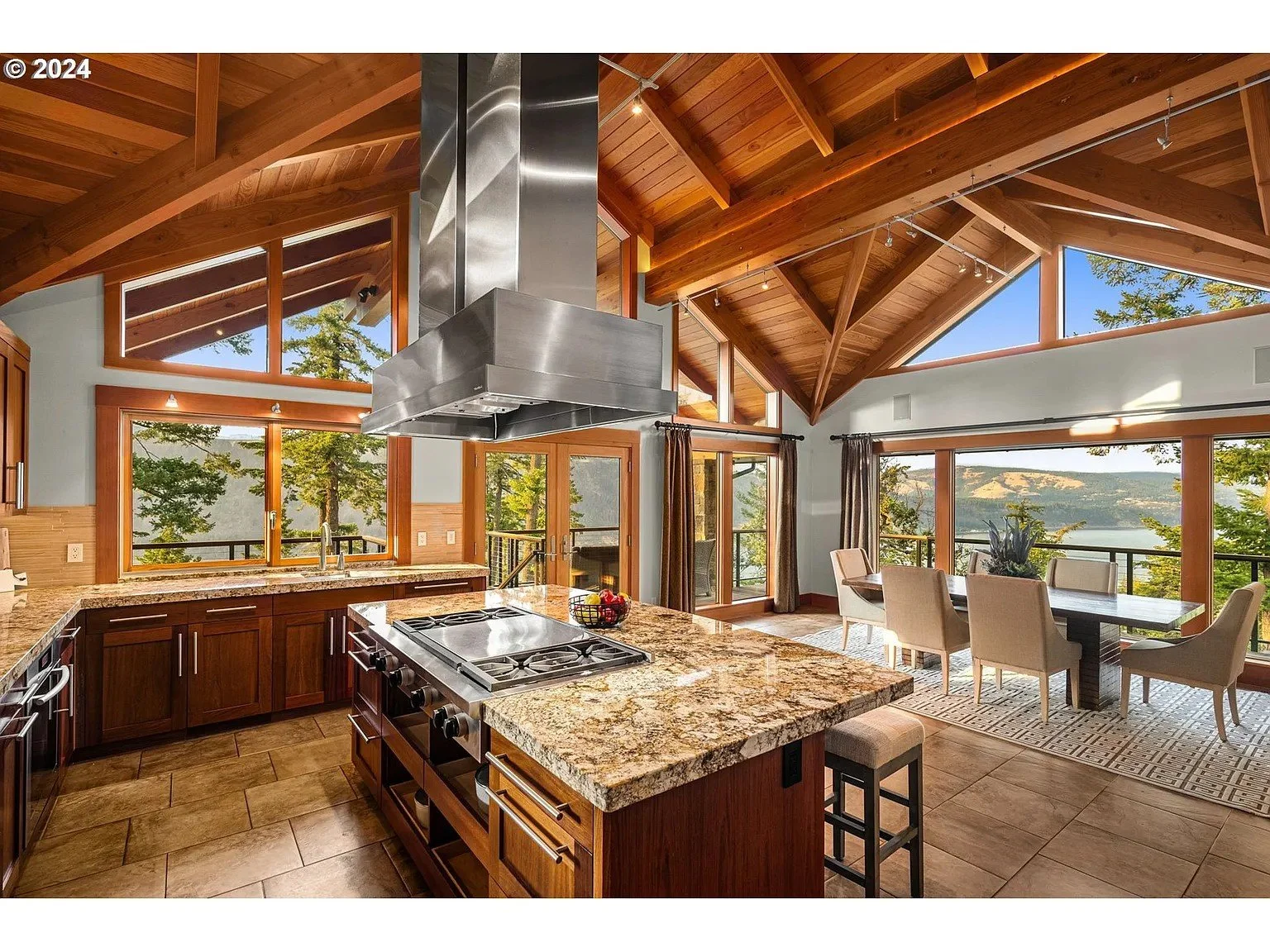 Modern kitchen and dining area with wooden beams, large windows, granite countertops, and nature view.
