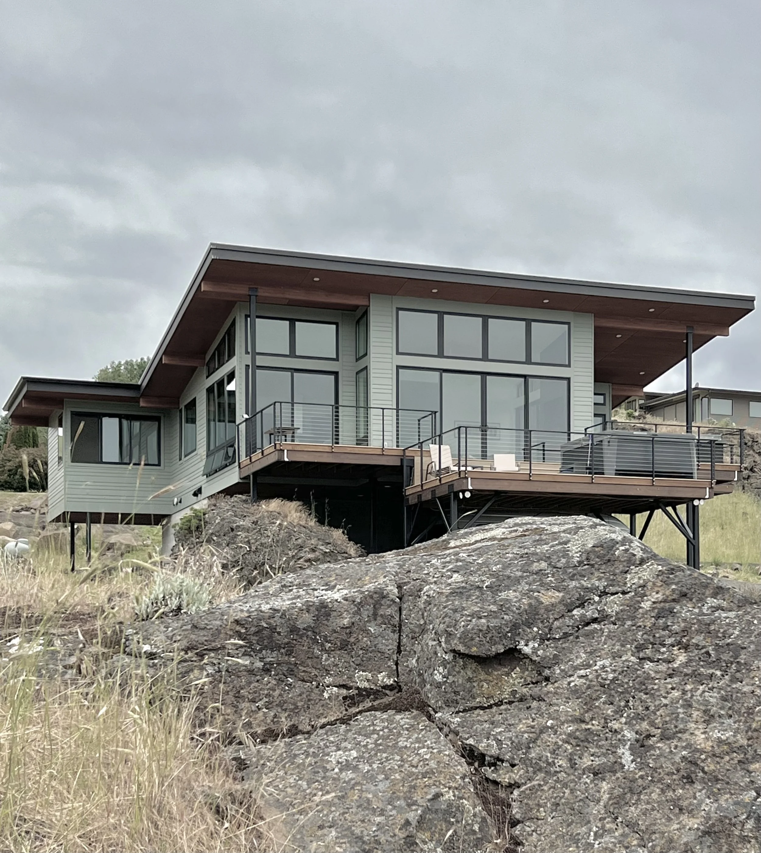 Modern house with large windows, elevated on stilts, surrounded by rocks and grass.