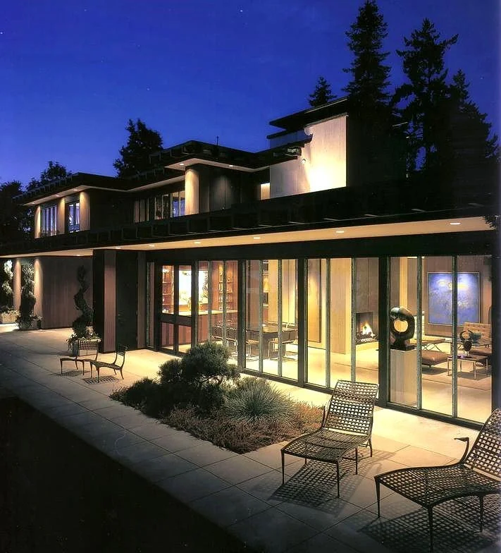 Modern house with glass windows at night, landscaped patio with chairs