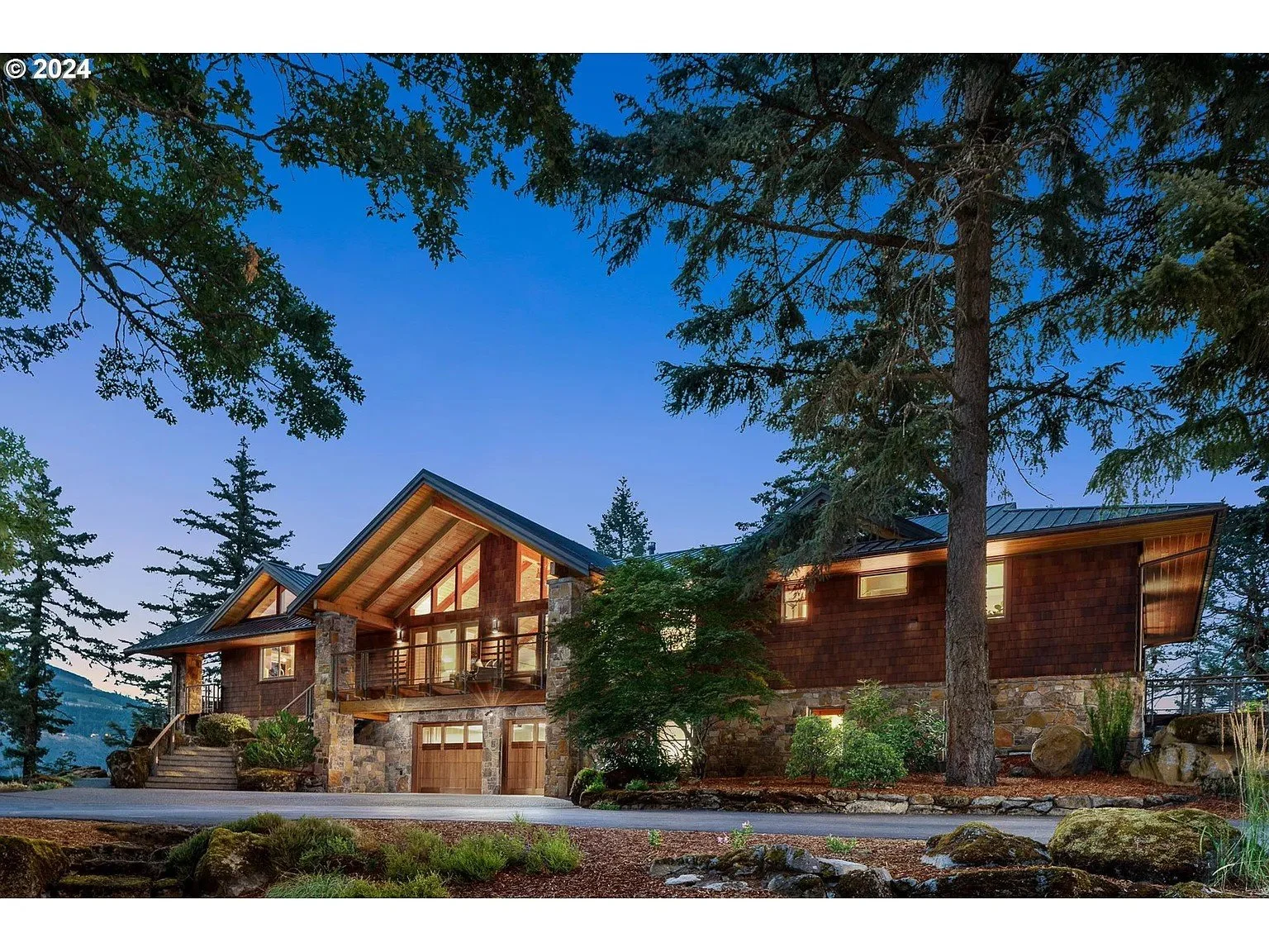 Luxury mountain house exterior at dusk with stone and wood façade, surrounded by trees.