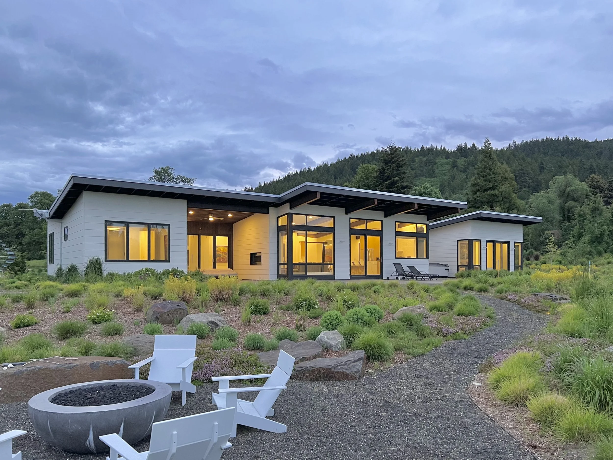 Modern house with large windows, surrounded by a landscaped garden and outdoor seating area with a fire pit.