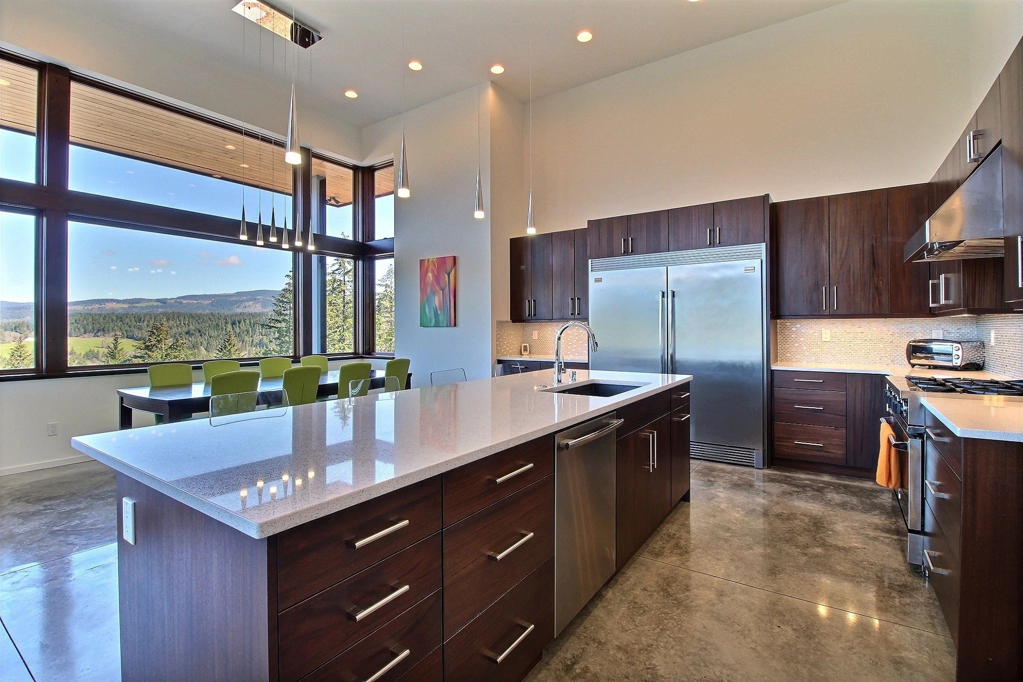 Spacious modern kitchen with large island, dark wood cabinets, stainless steel appliances, pendant lights, and scenic window view.