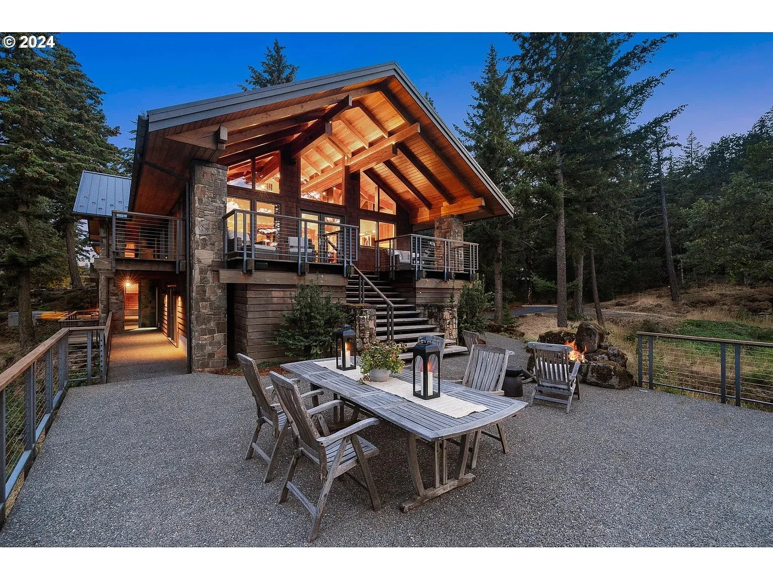 Rustic cabin with stone and wood exterior, elevated deck, outdoor seating area, fire pit, surrounded by trees.