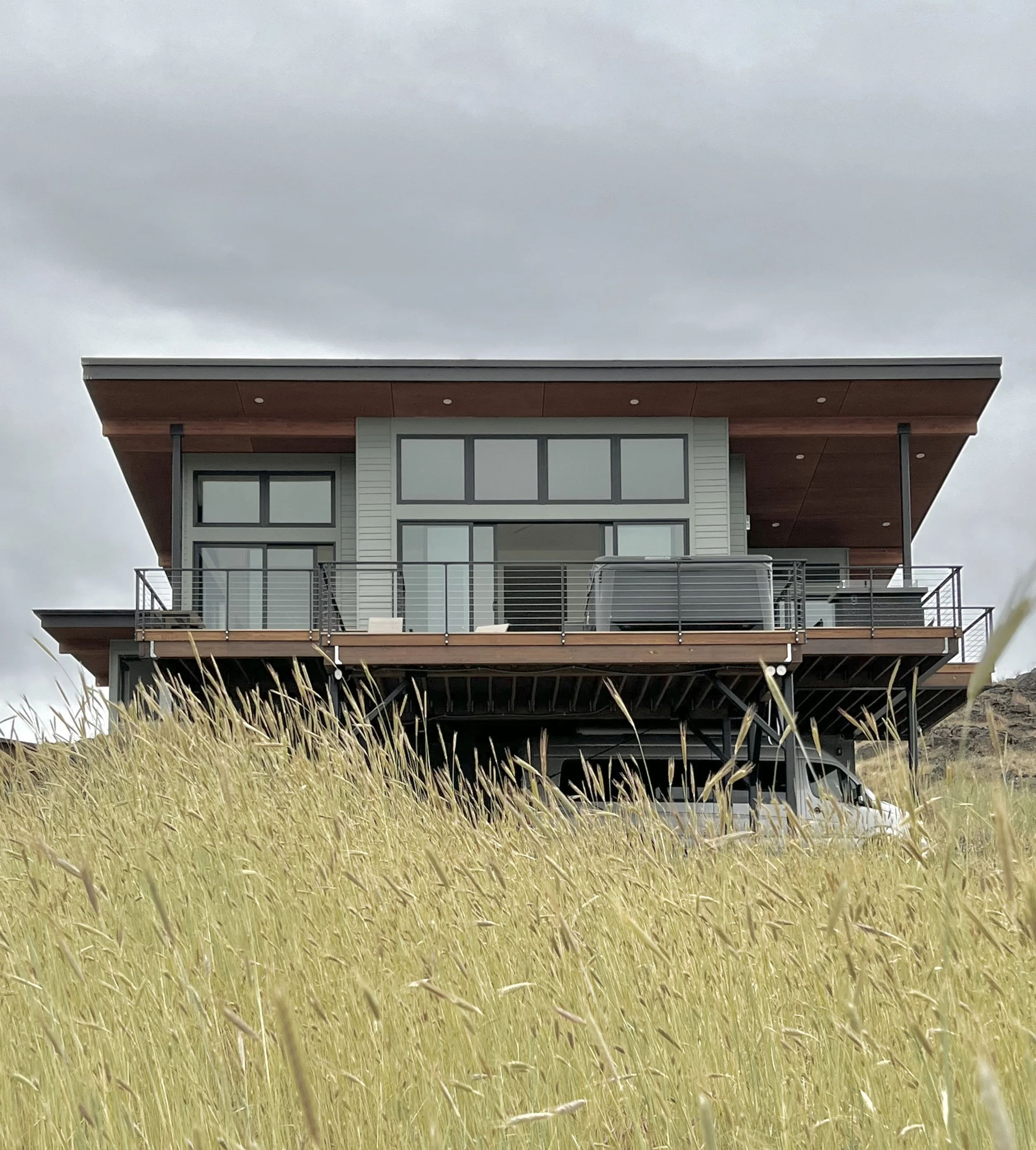 Modern house with large windows and balcony, set in tall grass landscape.