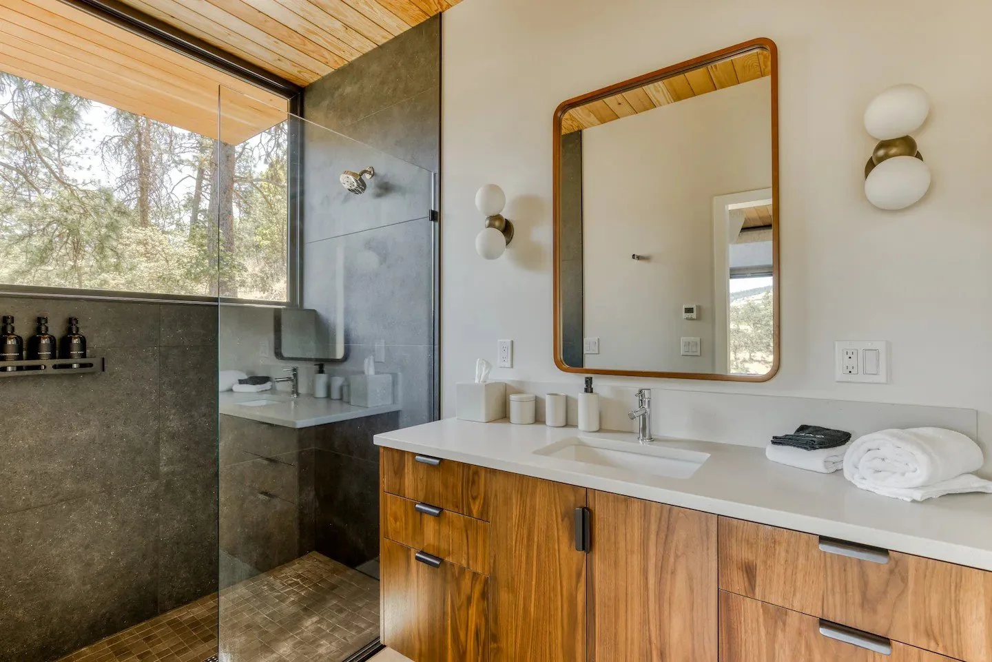 Modern bathroom with glass shower, wooden vanity, large mirror, and natural light