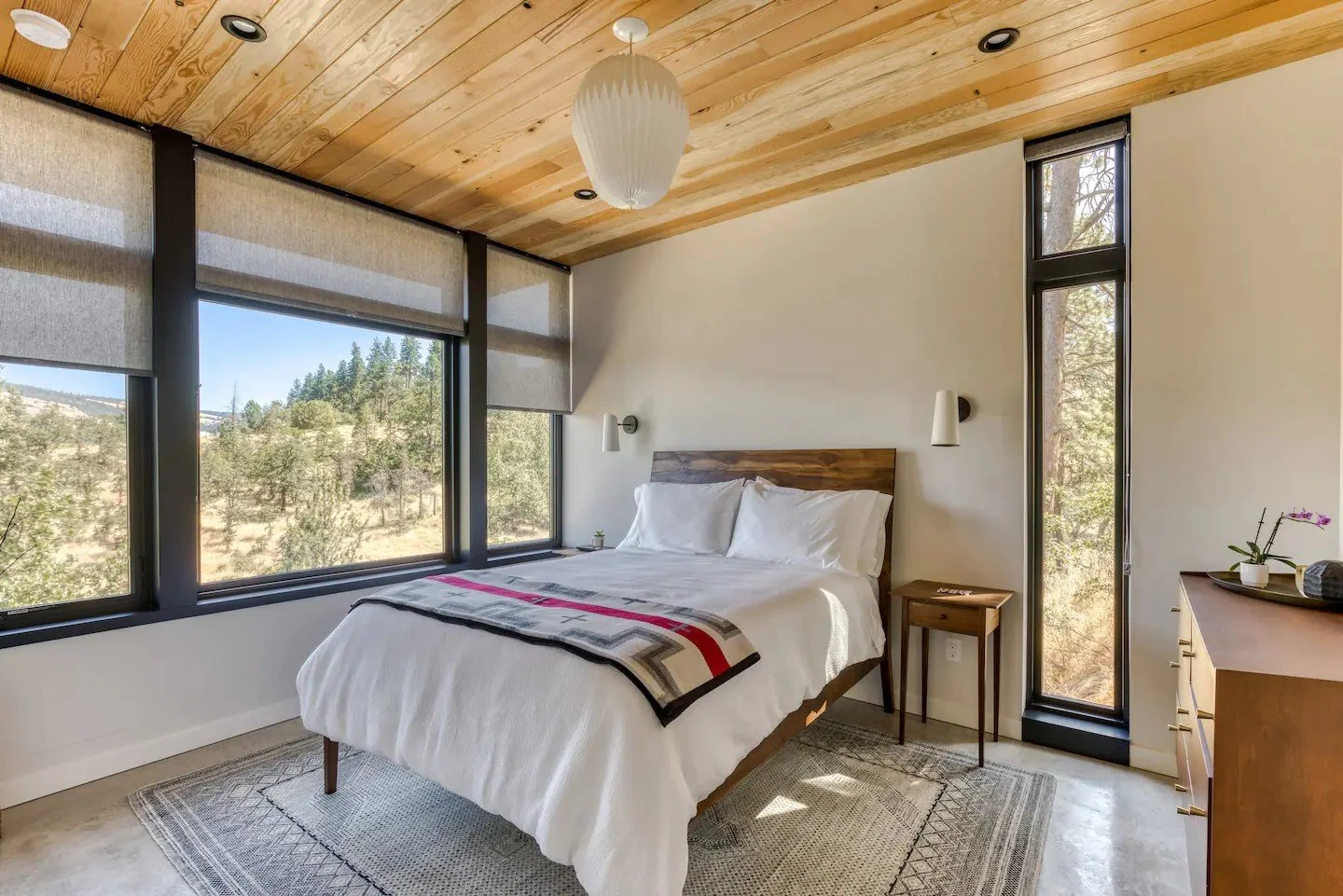 Modern bedroom with large windows, wood ceiling, and minimalist decor.