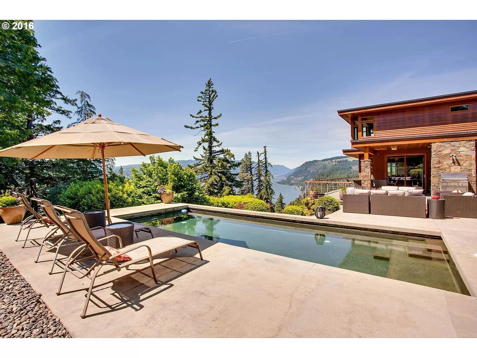 Outdoor pool area with loungers, umbrella, and scenic mountain view in the background.