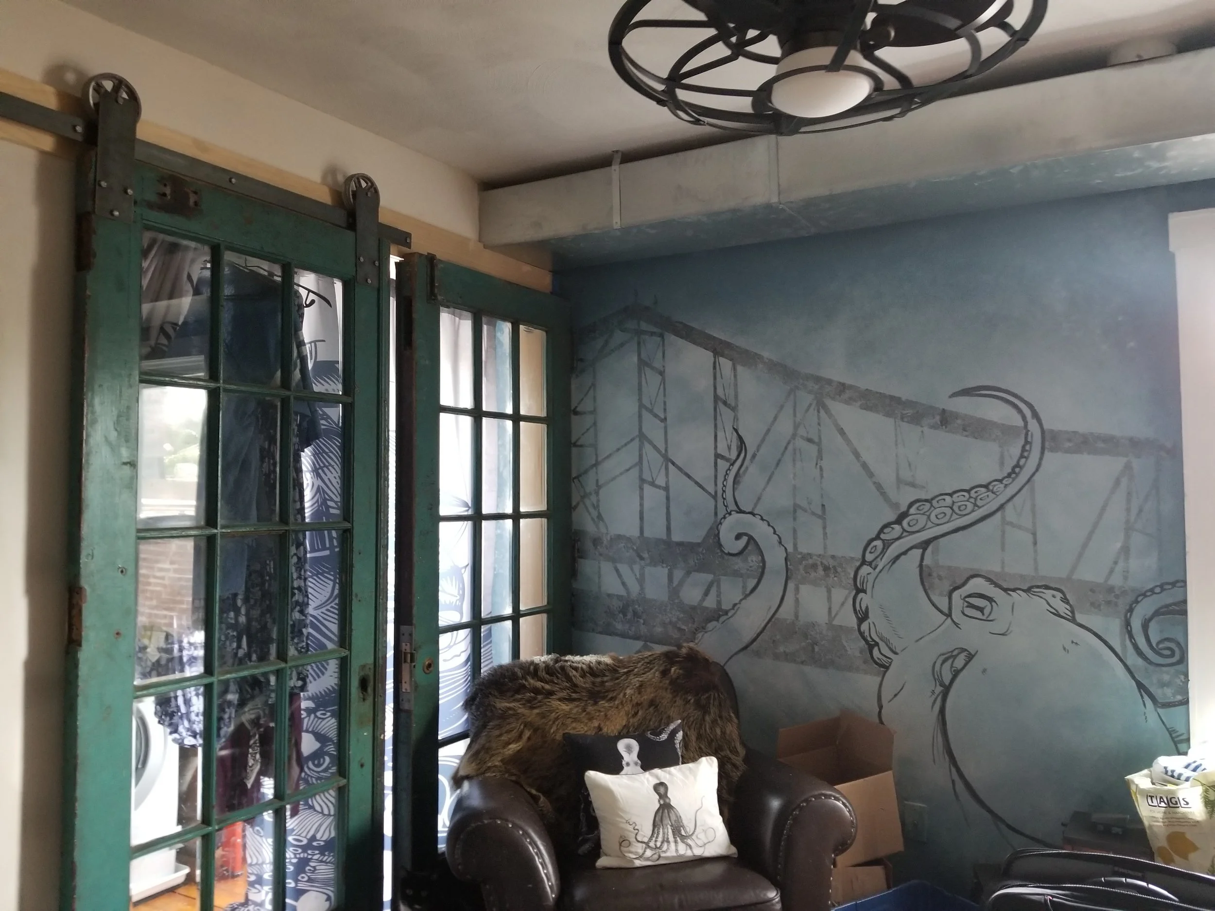 Interior with rustic sliding blue-green doors, octopus mural, brown armchair, and modern ceiling fan.