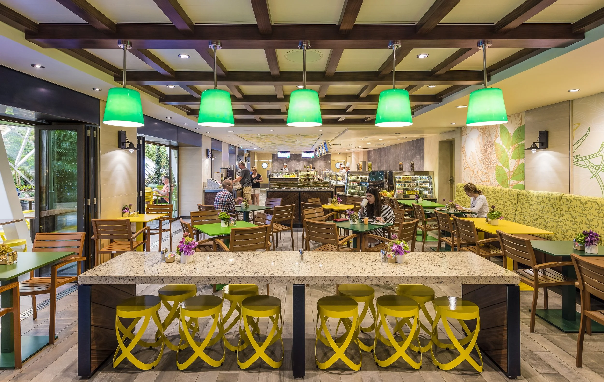 Modern cafe interior with green and yellow decor, wooden tables and chairs, and pendant lights.
