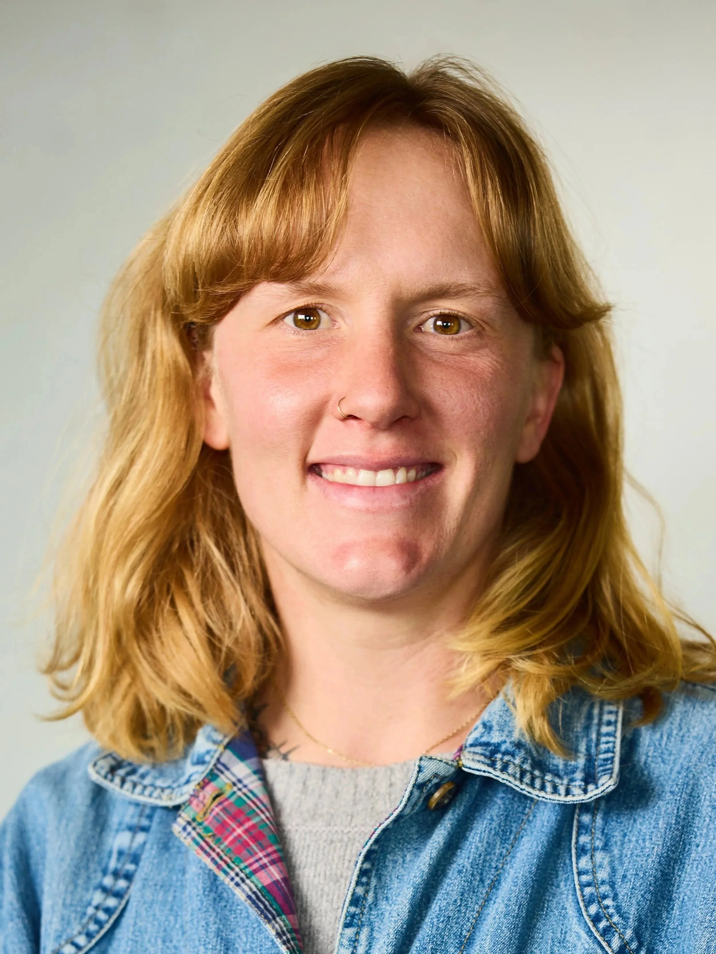 Woman smiling inside a greenhouse holding a child and a large basket of fresh lettuce and greens.
