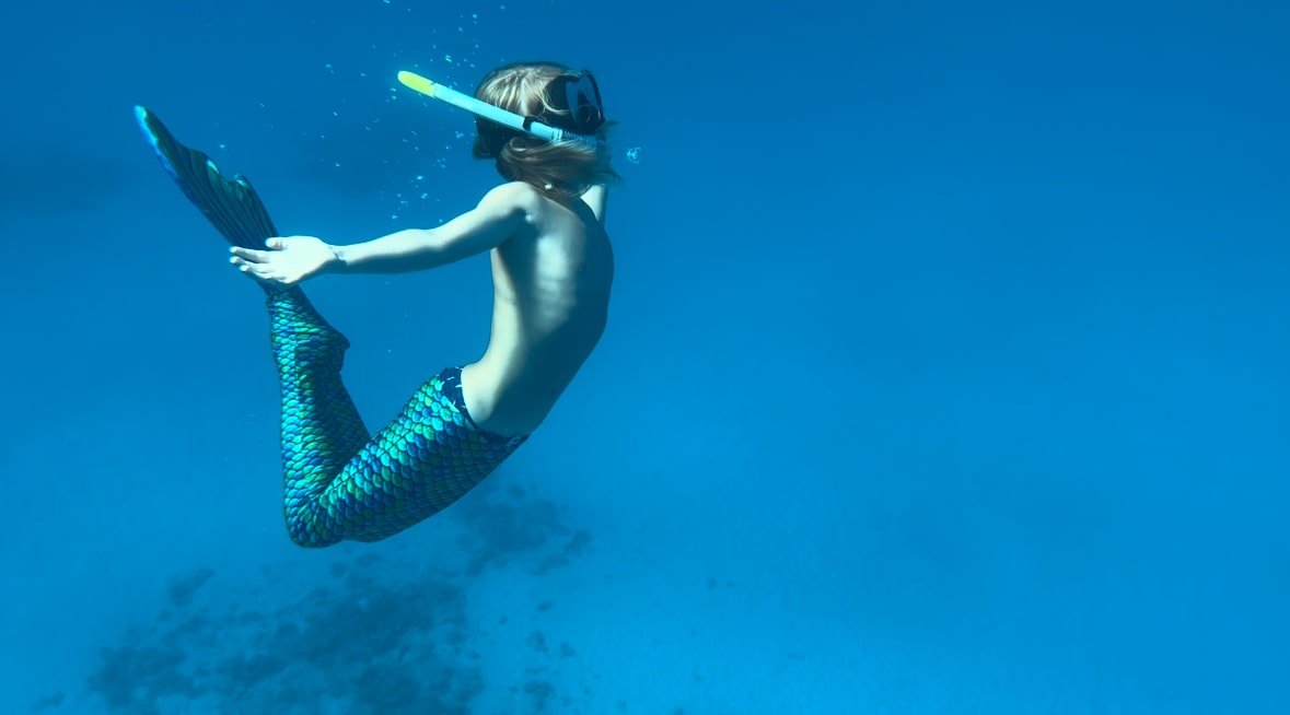 Person taucht im Wasser mit Schnorchel und Flossen, trägt eine schuppige Meerjungfrauenflosse. Unterwasserfotografie Felizitas Viola